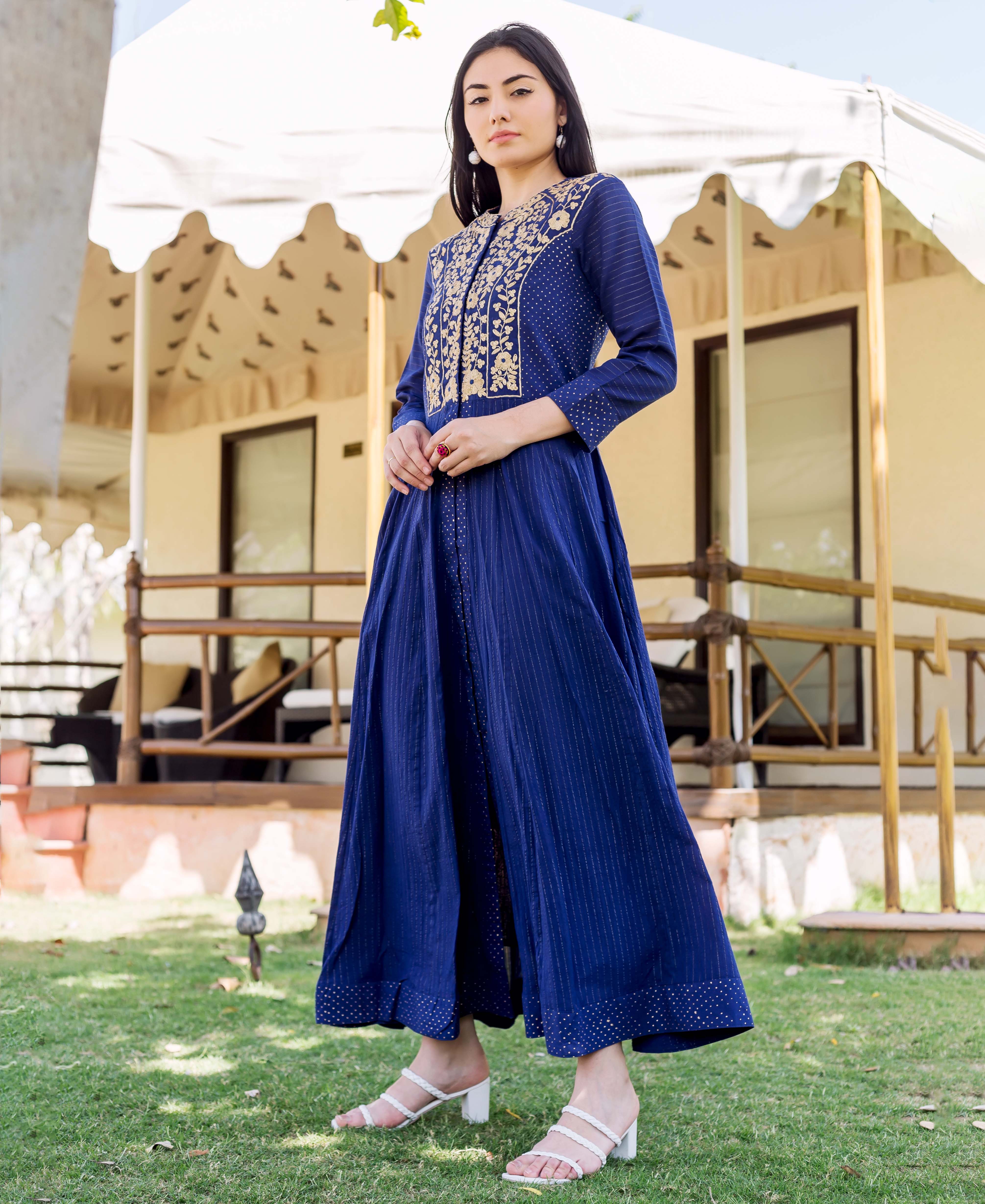 A woman in a royal blue dress with gold embroidery and white heels.