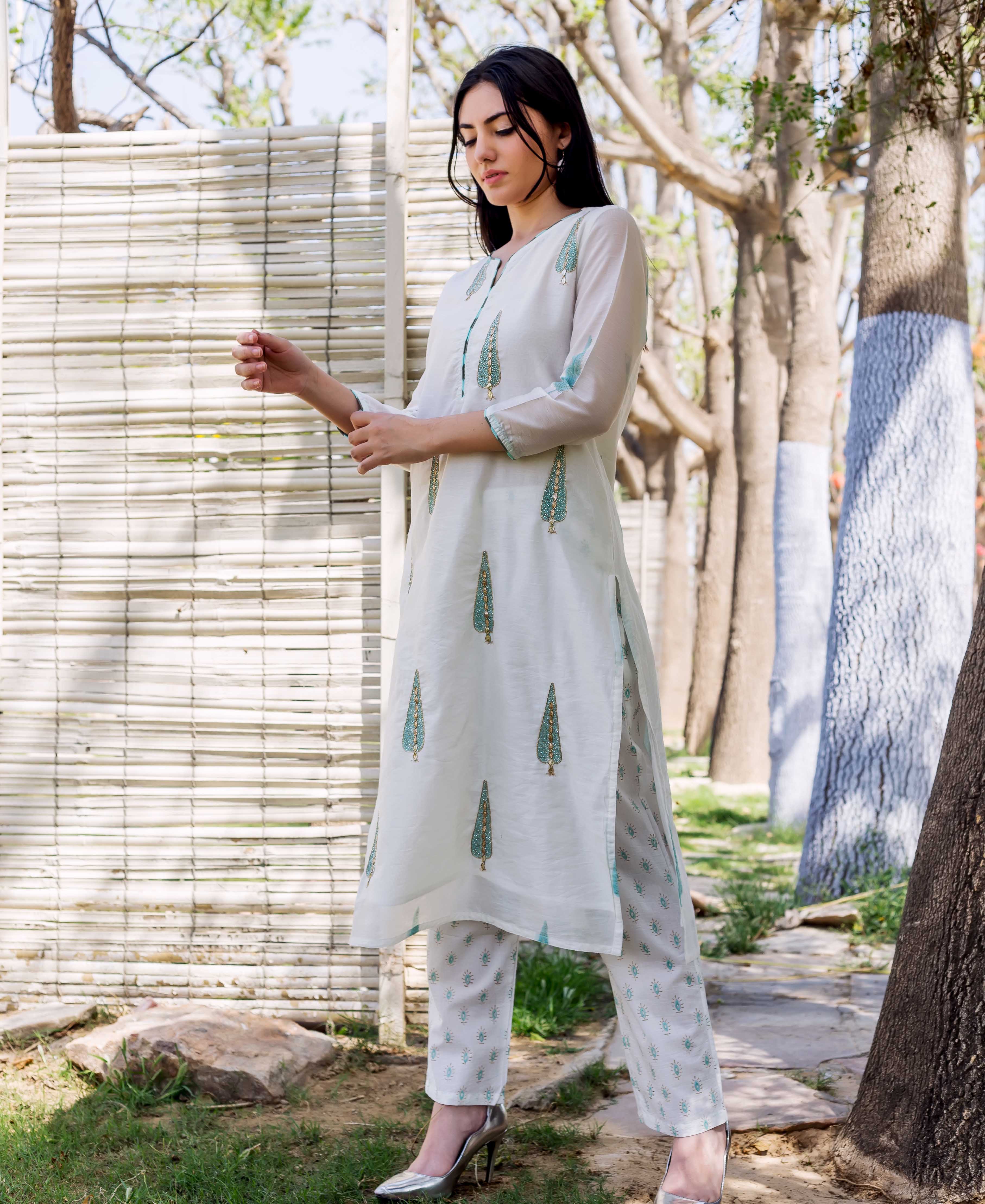 A woman in a white, hand-block-printed kurta with green and gold accents.