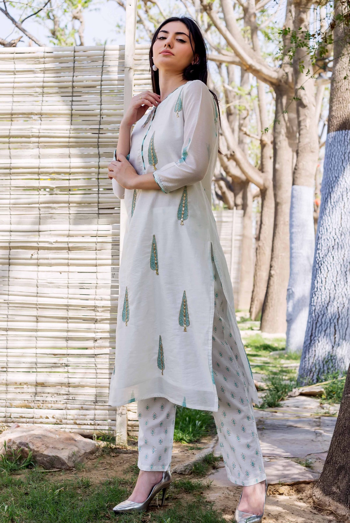 A woman in a white kurta with green and gold block prints, standing outdoors.