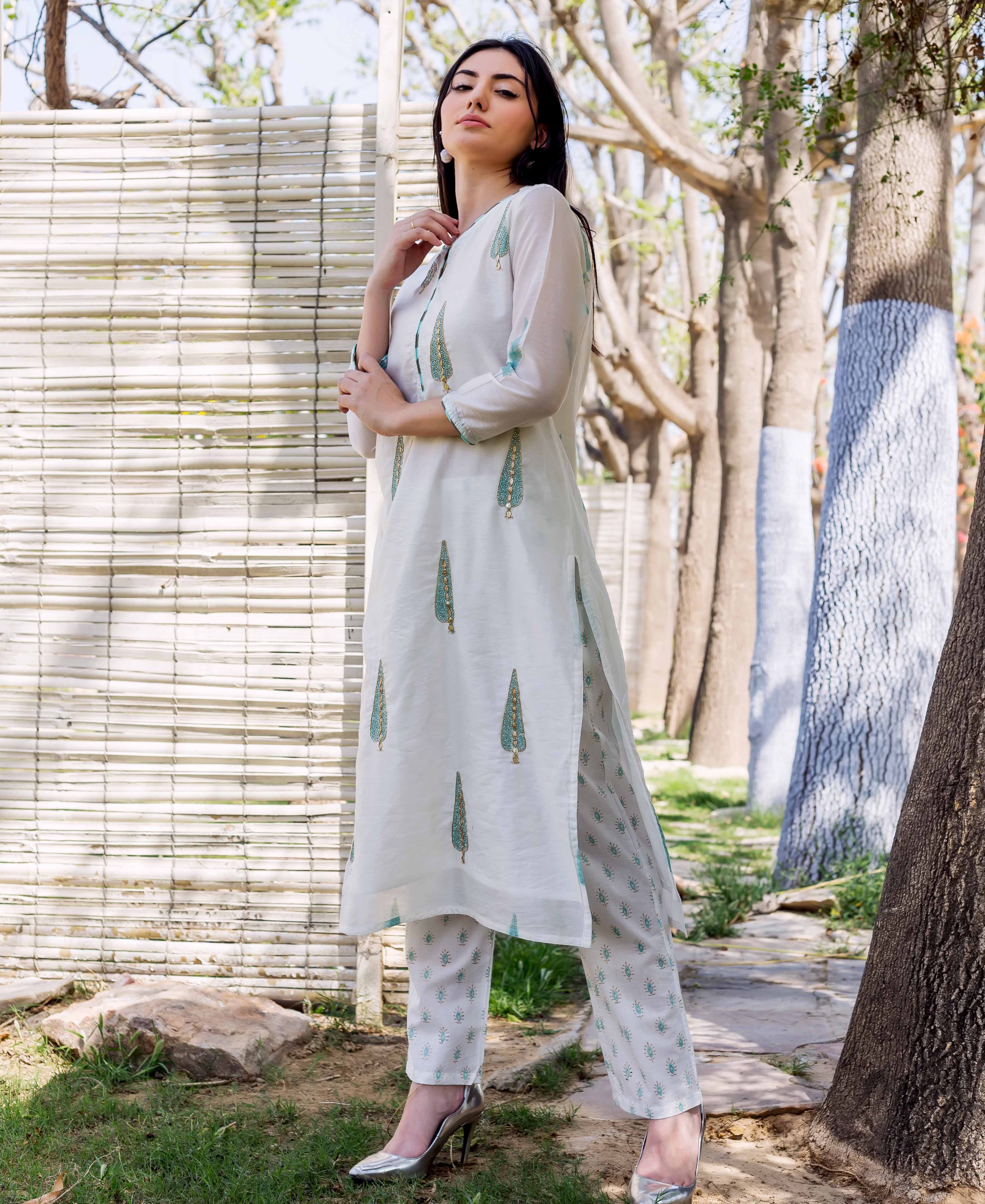A woman in a white kurta with green and gold block prints, standing outdoors.