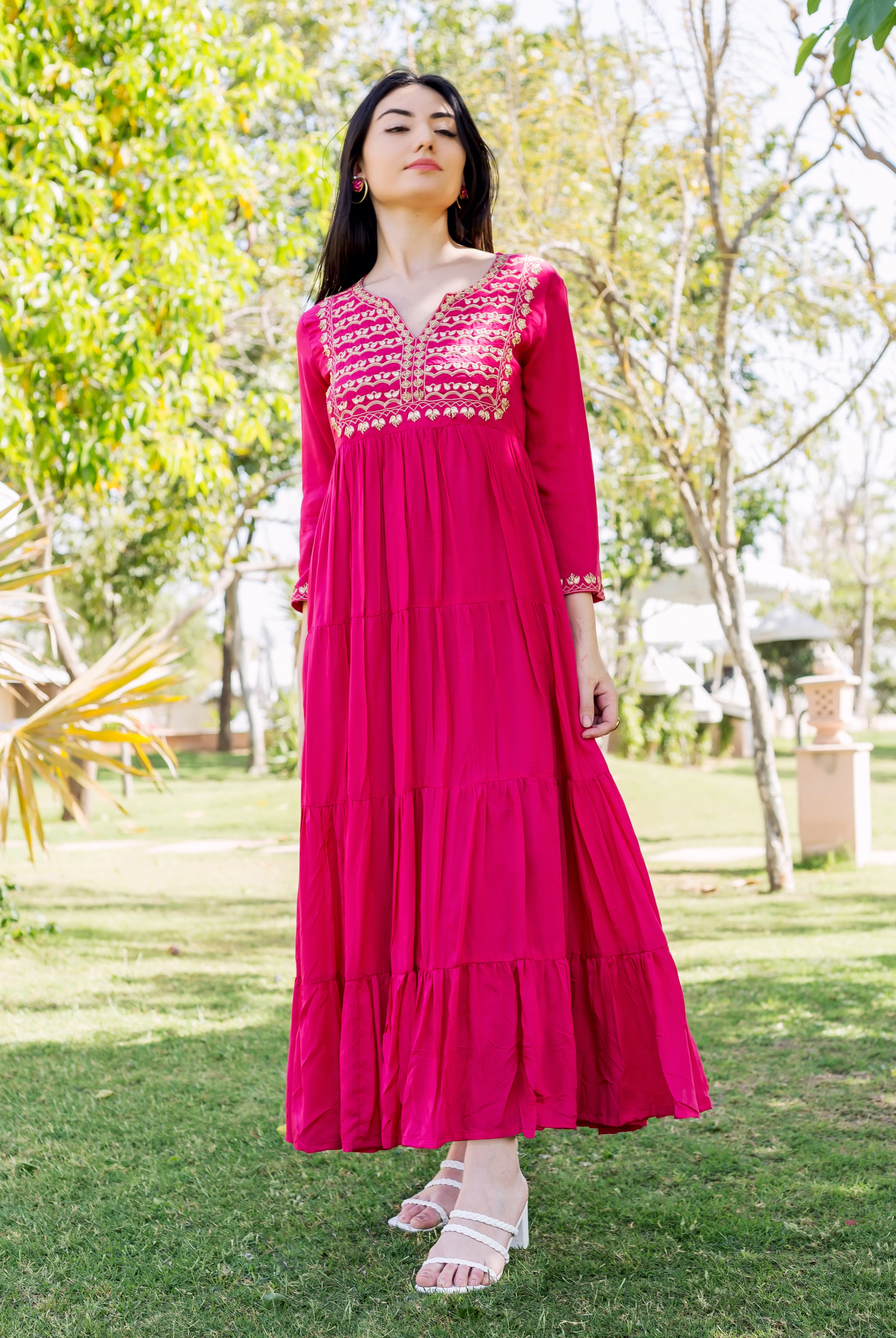 Front view of model wearing Aaditri Raspberry Red tiered dress with intricate gold embroidery.
