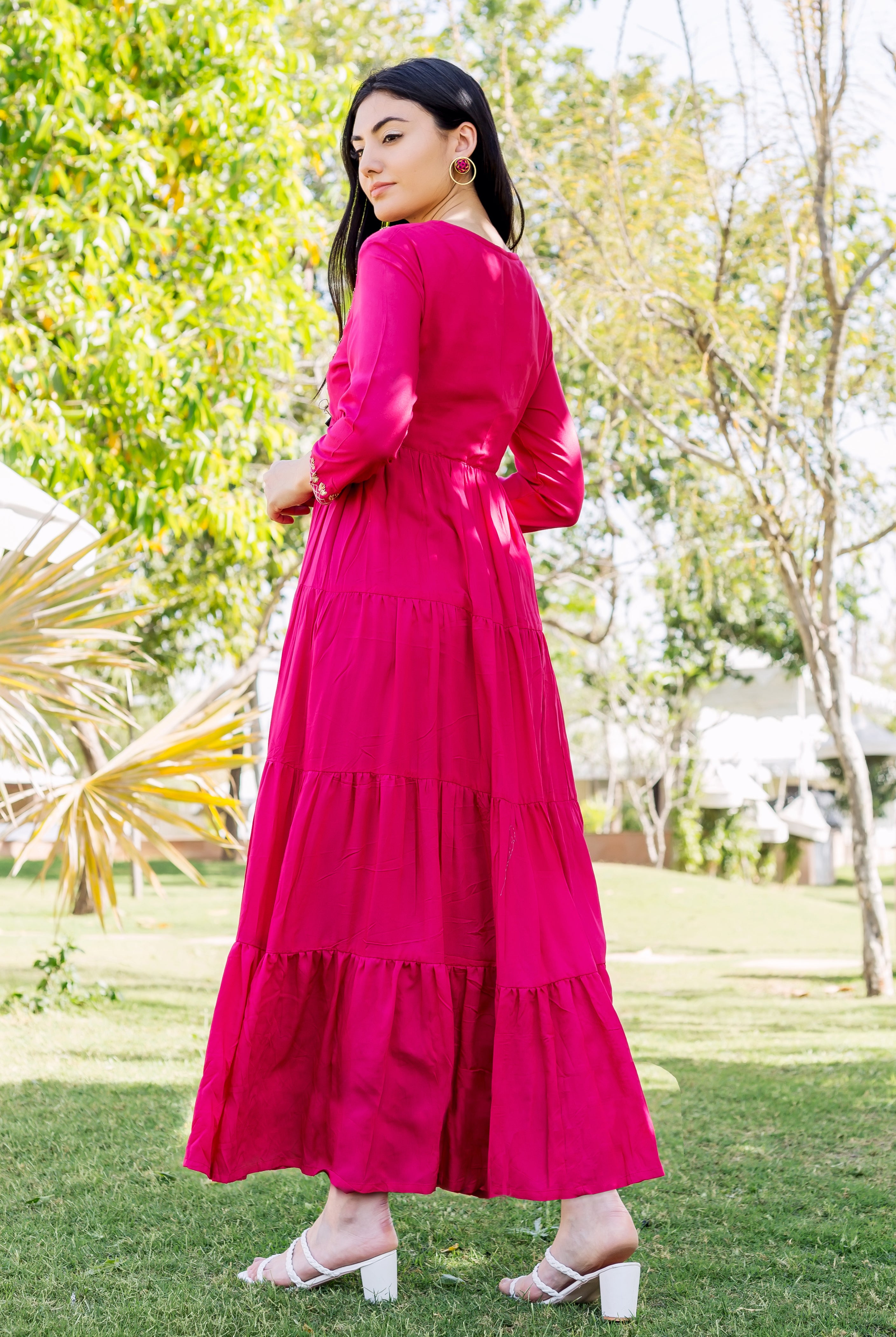 A woman in a long, raspberry red dress with tiered skirt and embroidered details.
