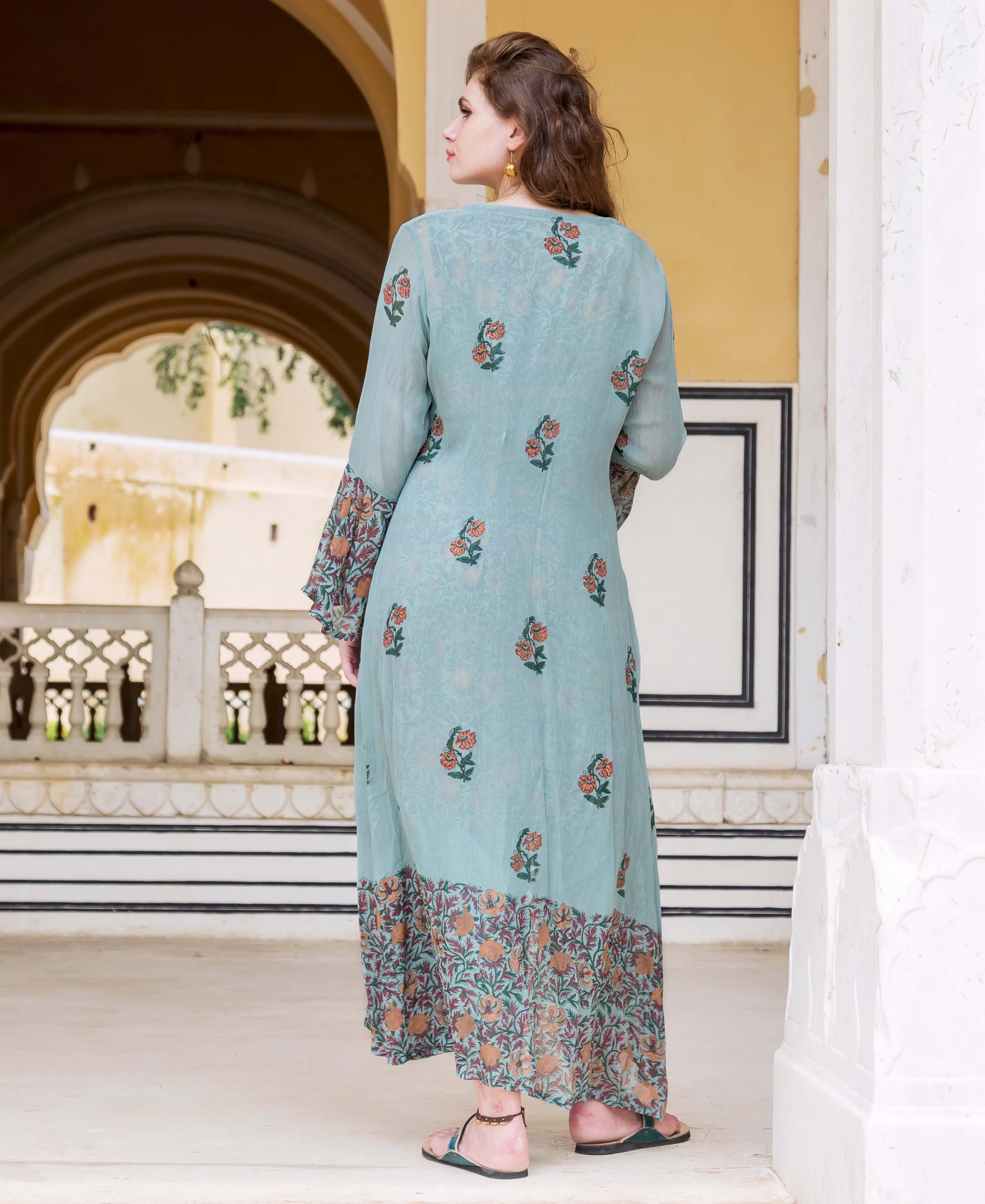A model wearing a long, light blue dress with floral patterns and a matching jacket.