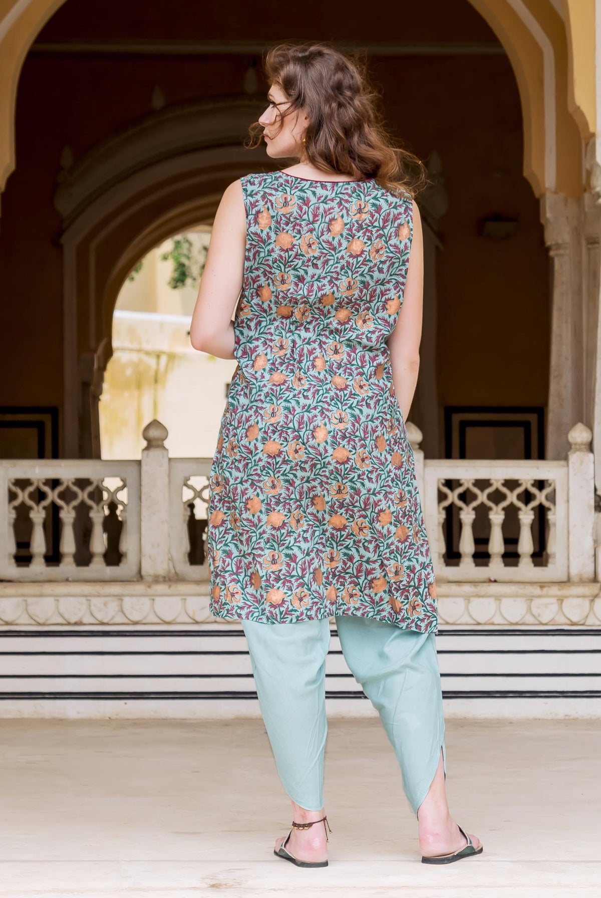 Model's back in Turkish blue sleeveless kurta with orange botanical print, and light blue dhoti.