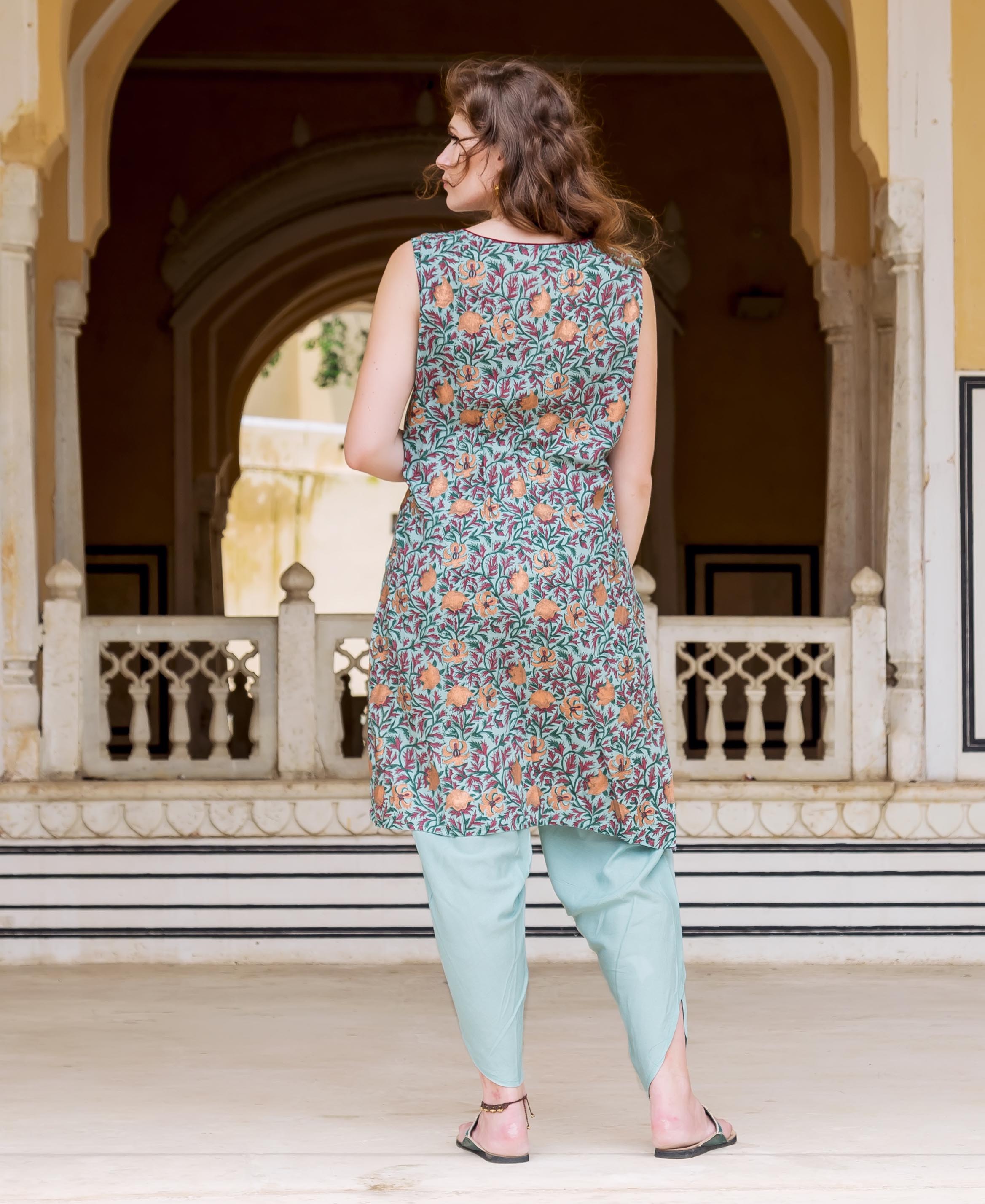 Model's back in Turkish blue sleeveless kurta with orange botanical print, and light blue dhoti.