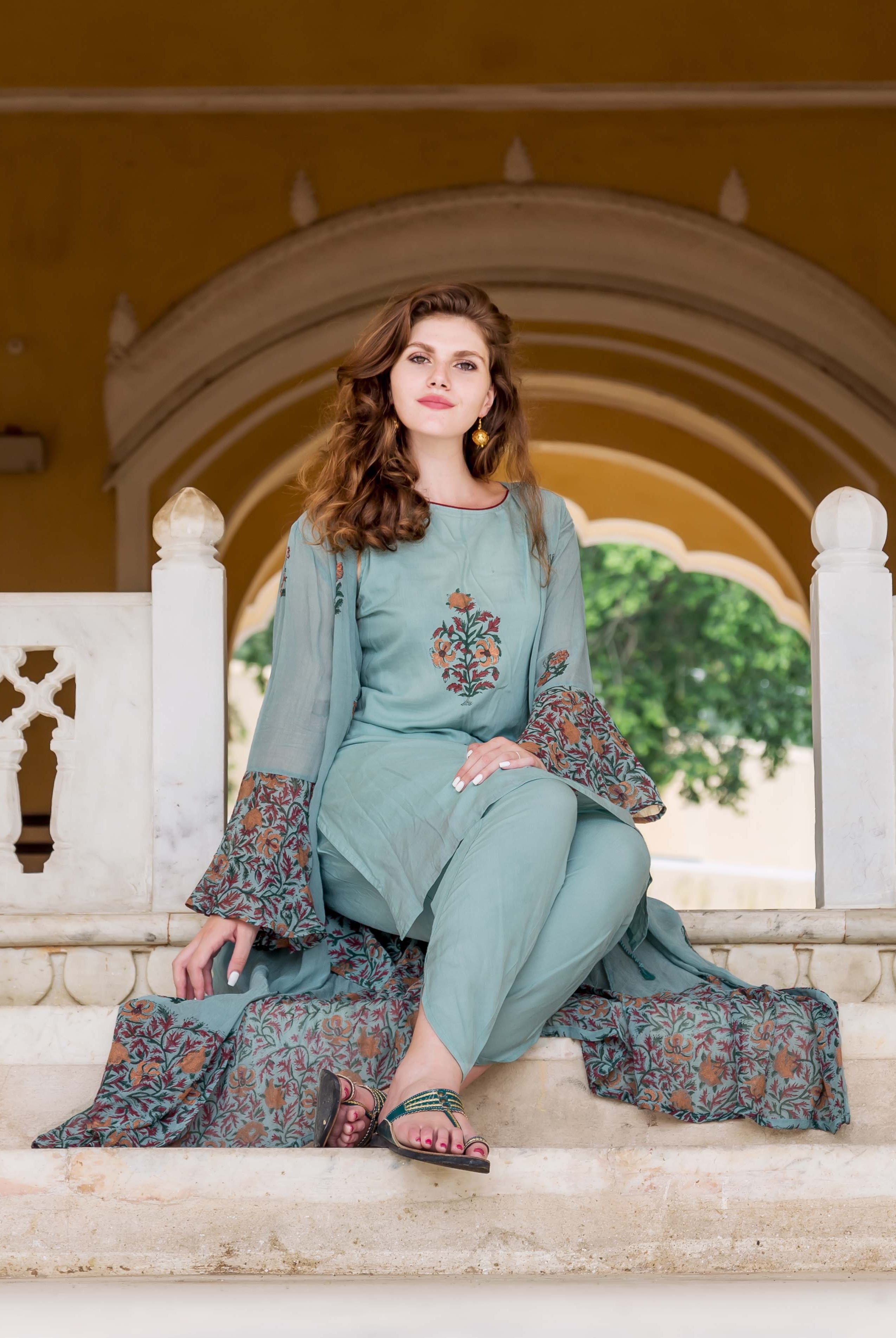 Woman in blue hand-block-printed dhoti set with jacket, sitting on steps.