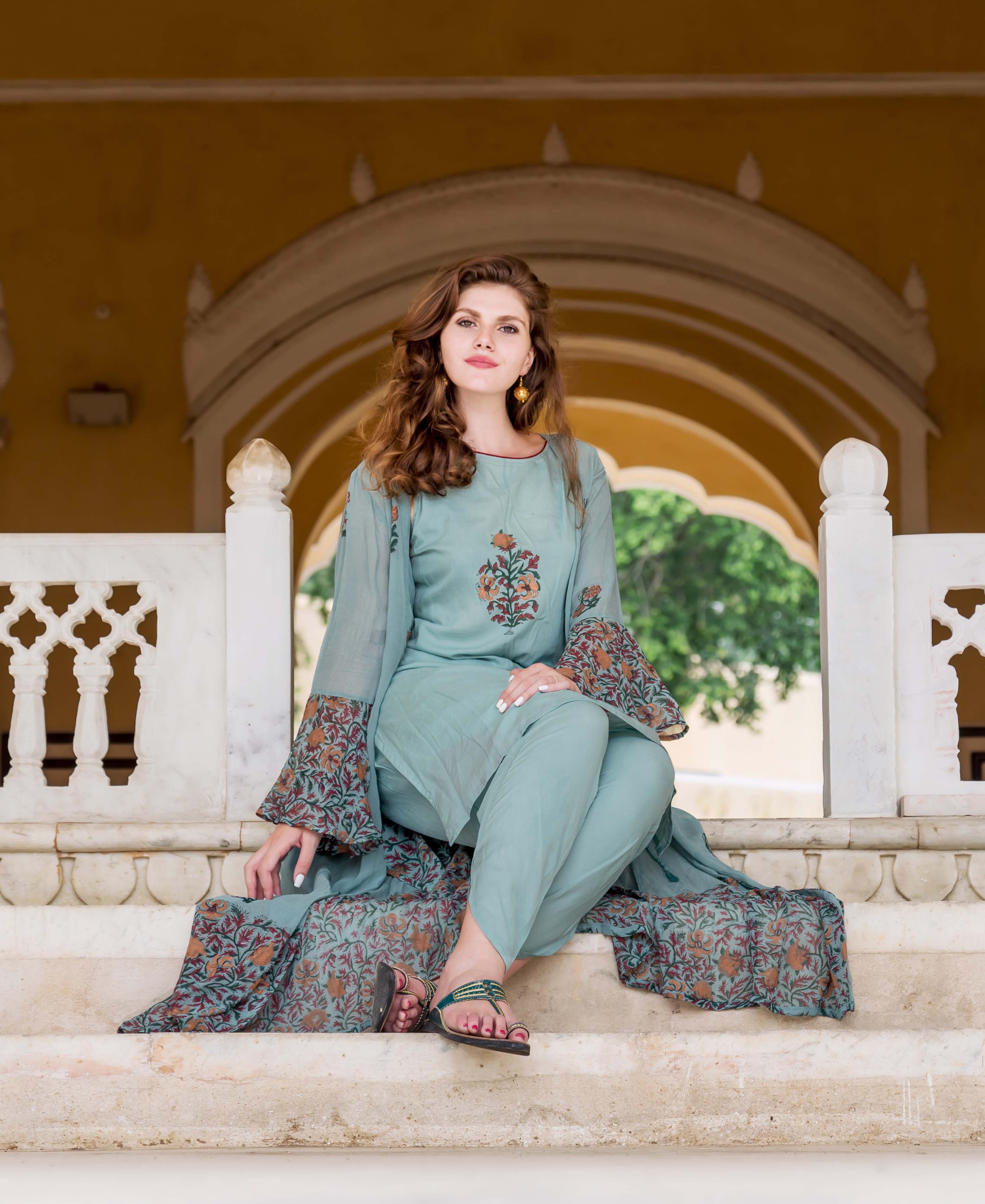 Woman in blue hand-block-printed dhoti set with jacket, sitting on steps.