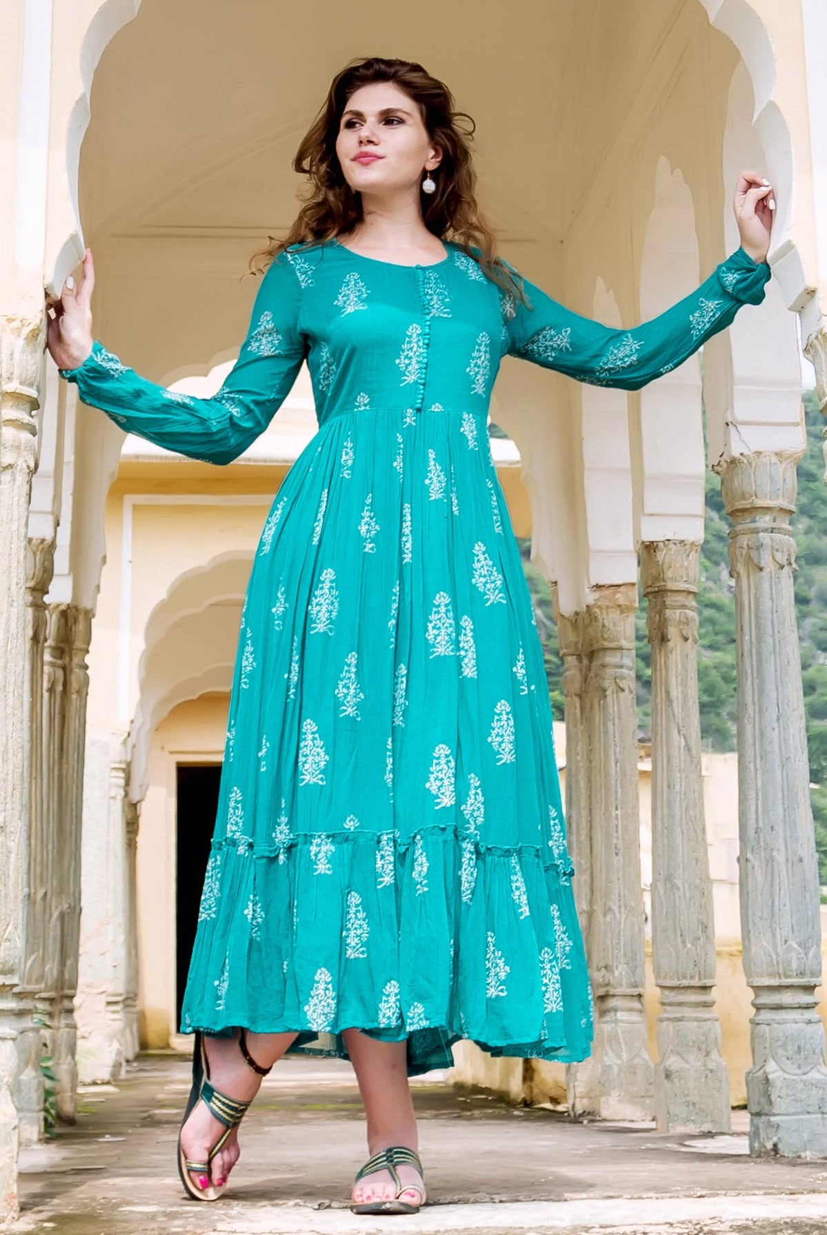Teal dress with white floral print, long sleeves and ruffled hem on a female model.