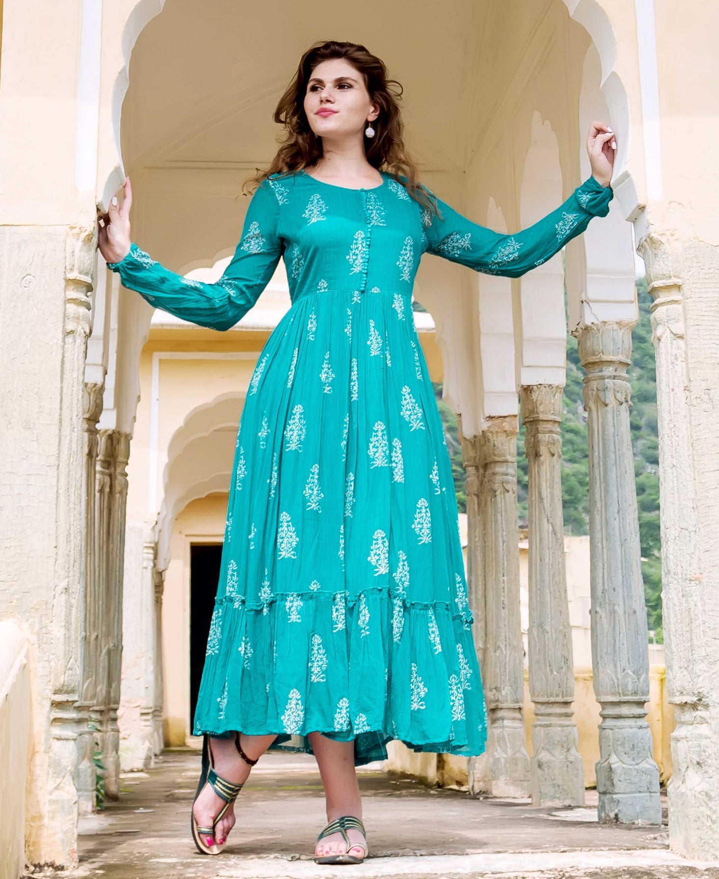 Teal dress with white floral print, long sleeves and ruffled hem on a female model.