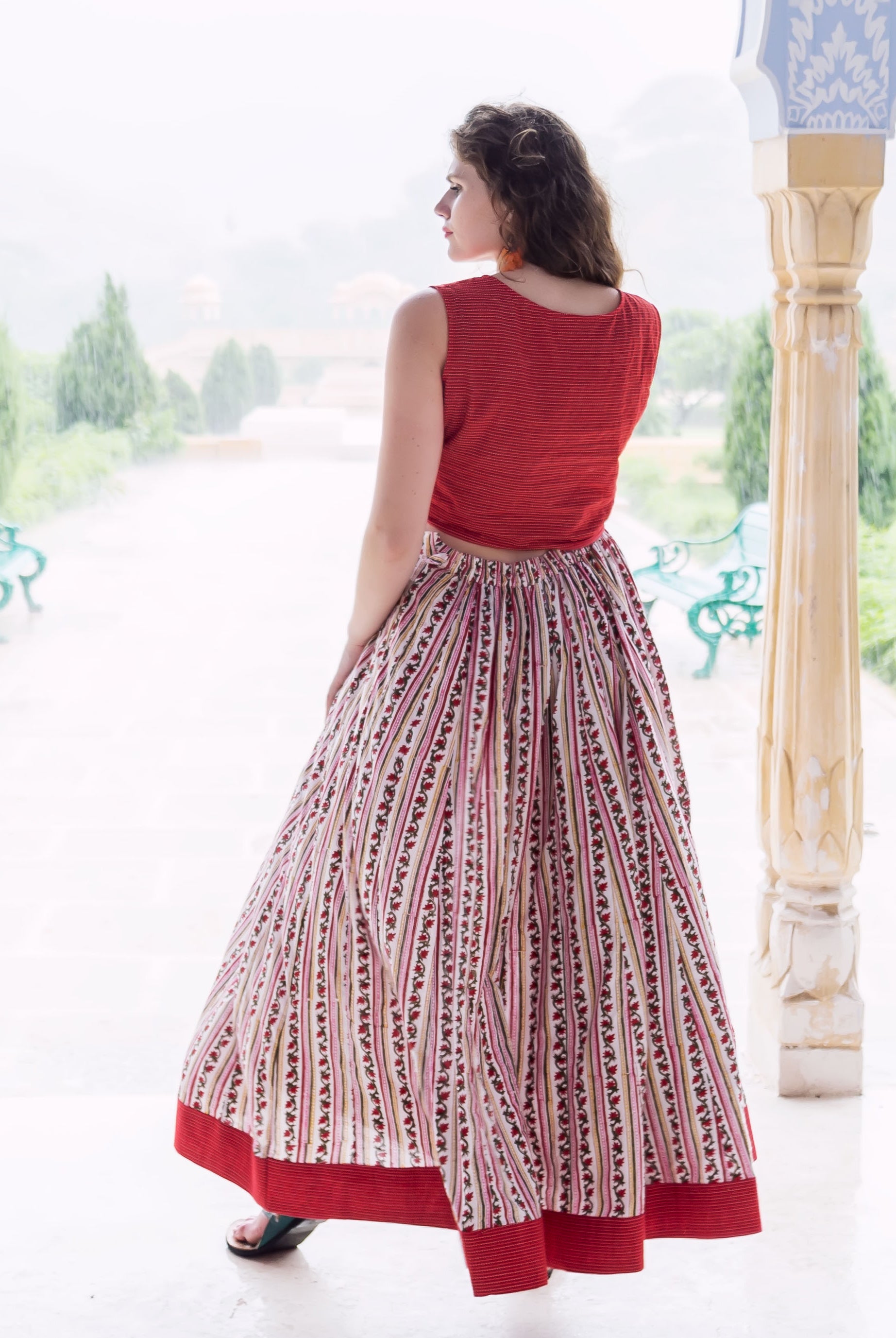 Model from back in red sleeveless crop top and white block-printed ethnic skirt.
