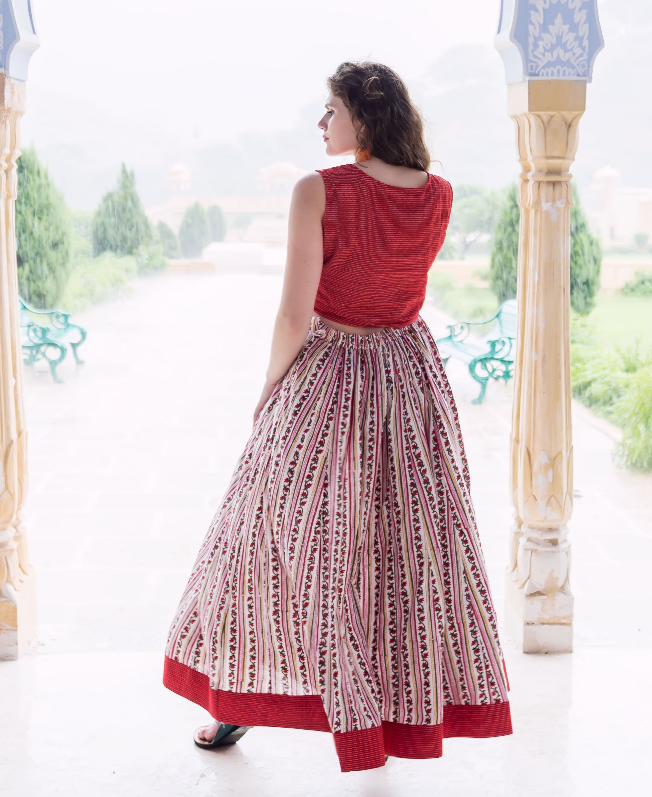 Model from back in red sleeveless crop top and white block-printed ethnic skirt.