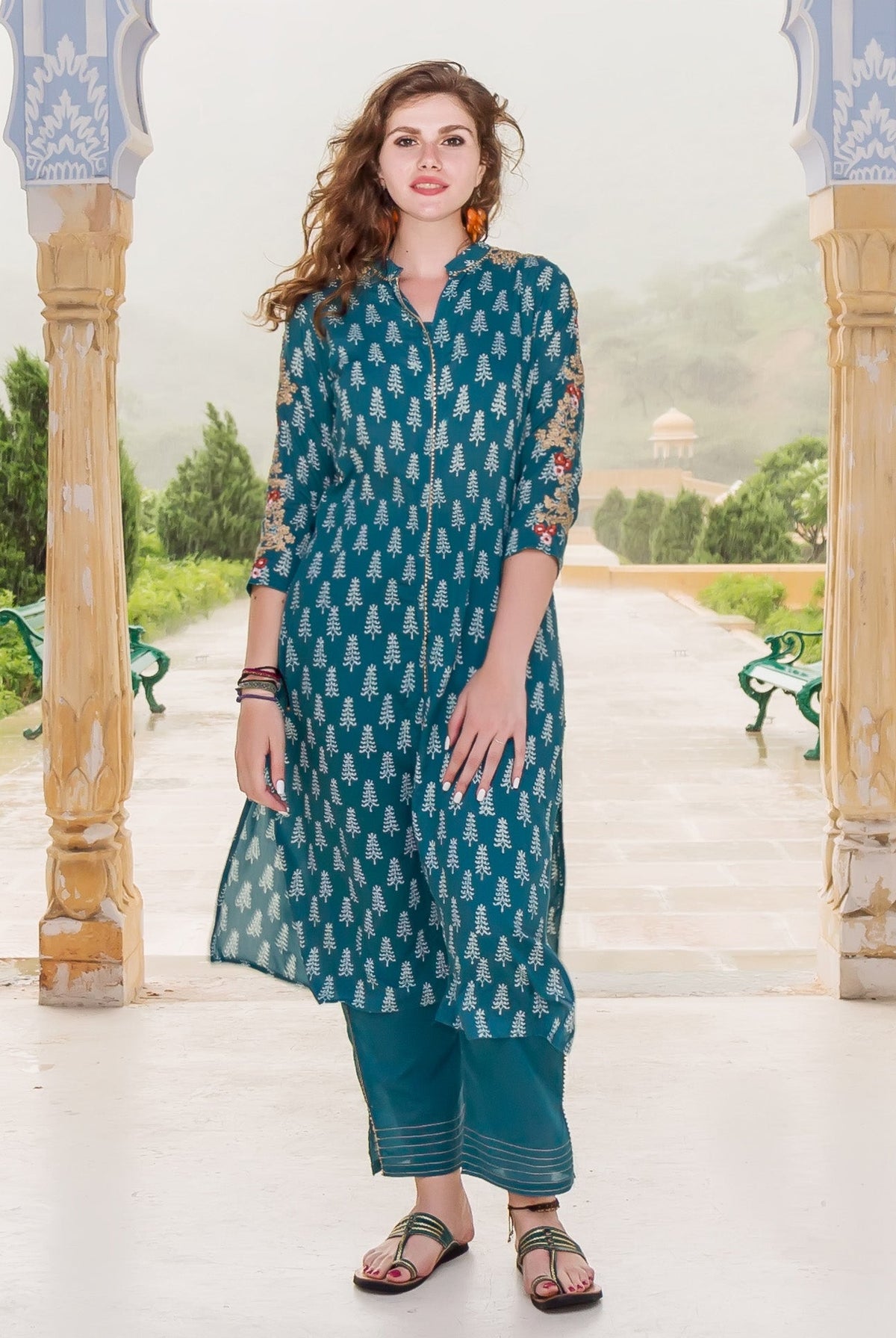 A model wearing a teal kurta with white tree print and floral embroidery on the sleeves.