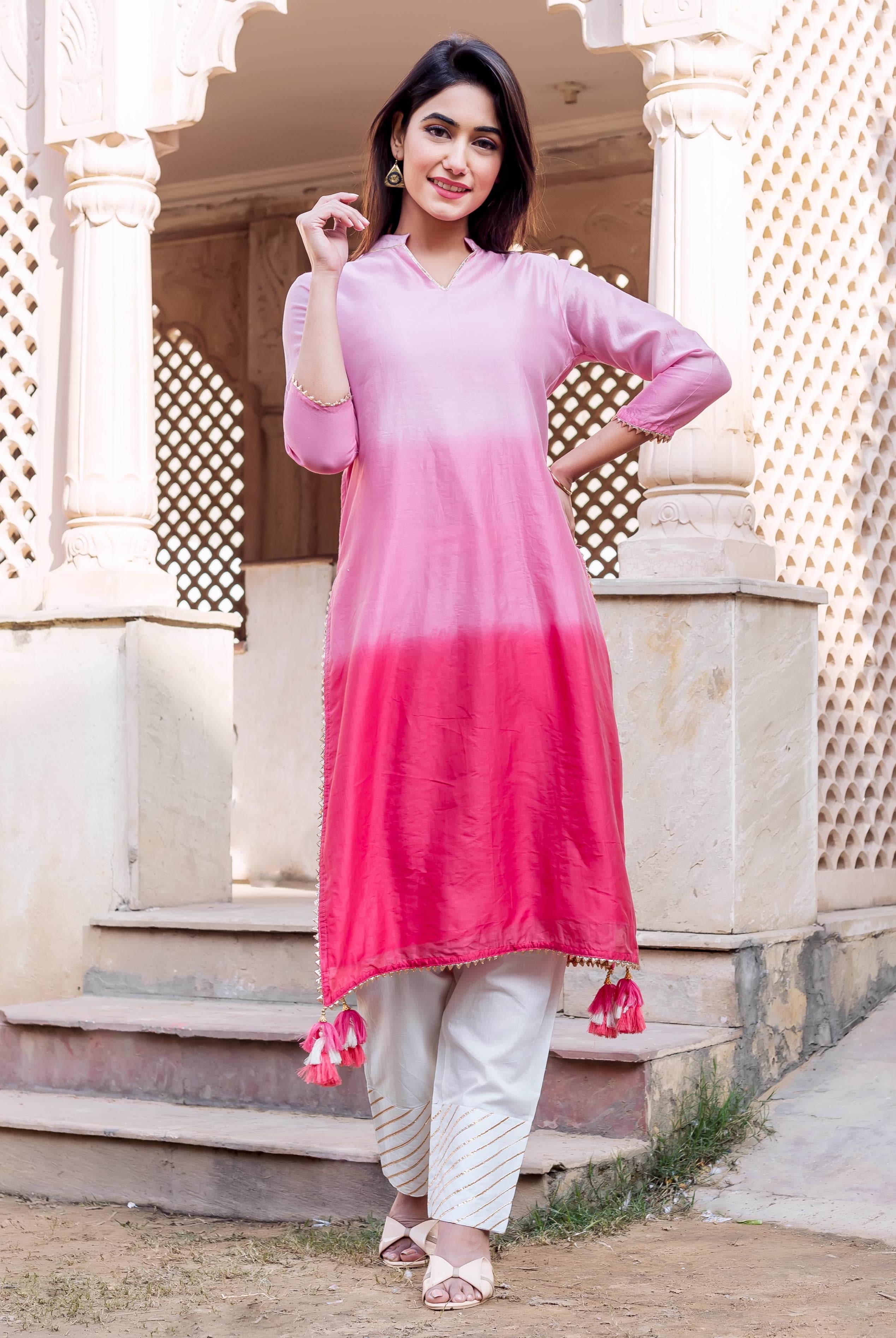 Full-length photo of a woman in ombre pink kurta and white pants with golden stripes.