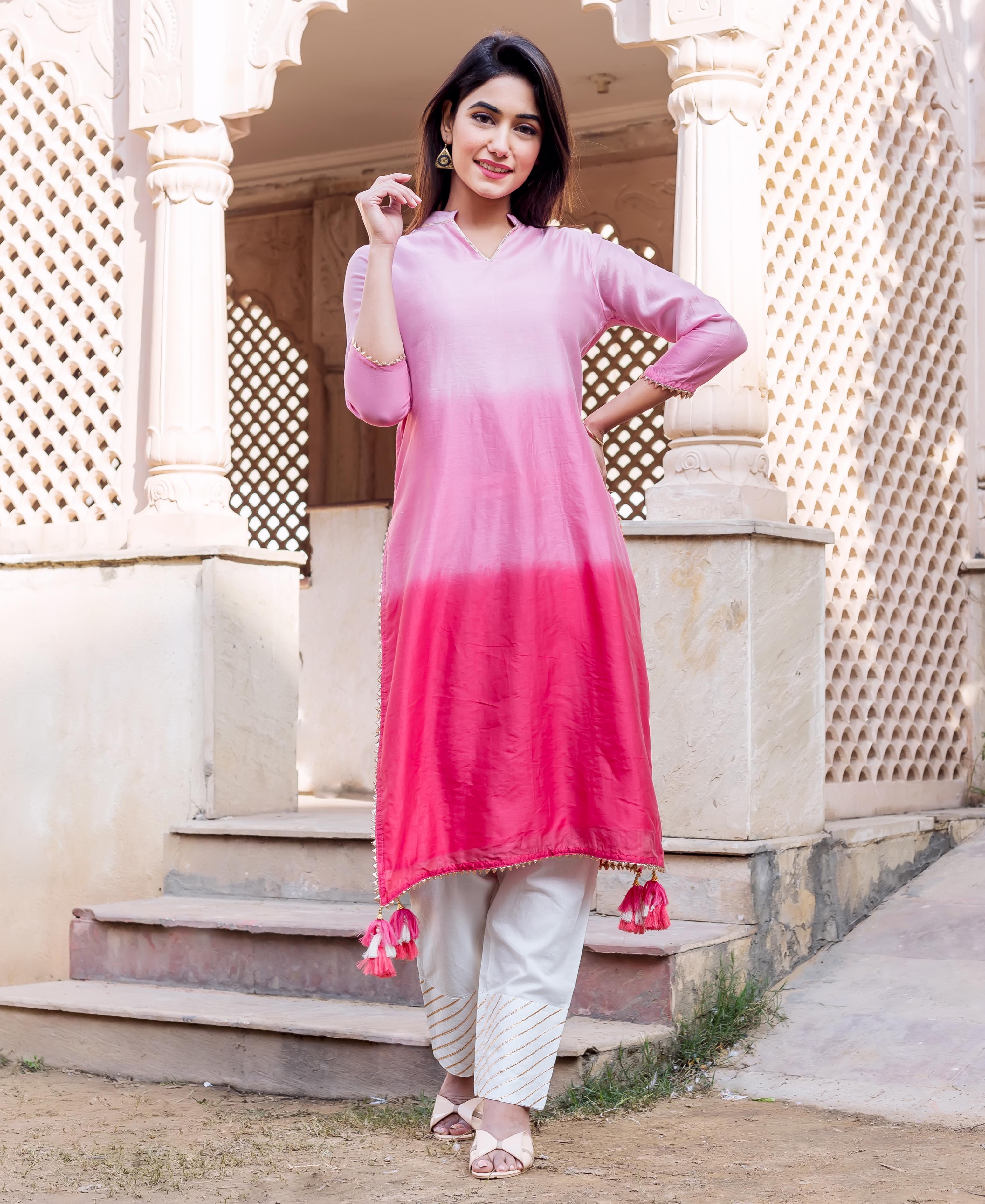 Full-length photo of a woman in ombre pink kurta and white pants with golden stripes.