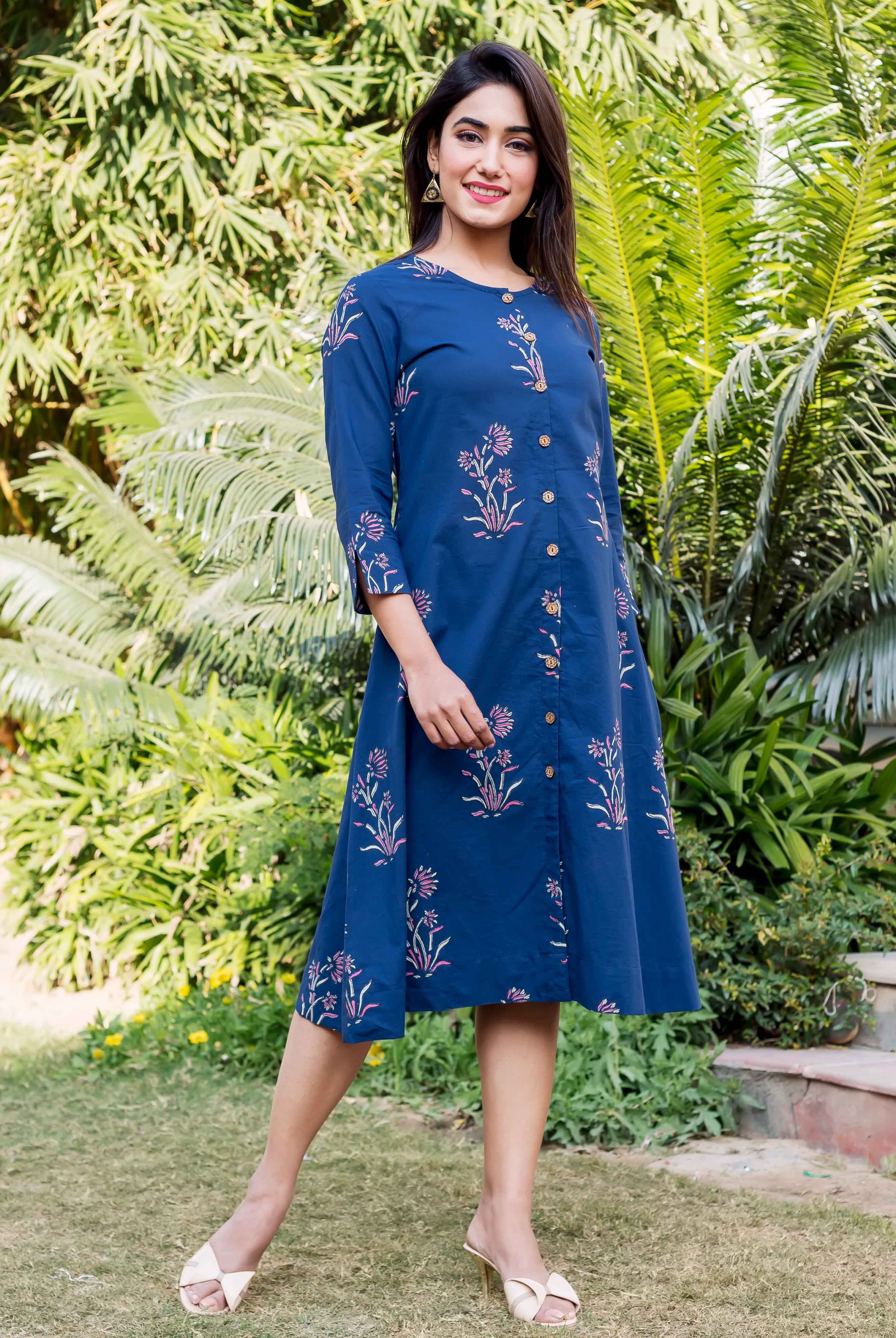 Model wears indigo knee-length dress featuring hand-block printed pink and green floral designs.