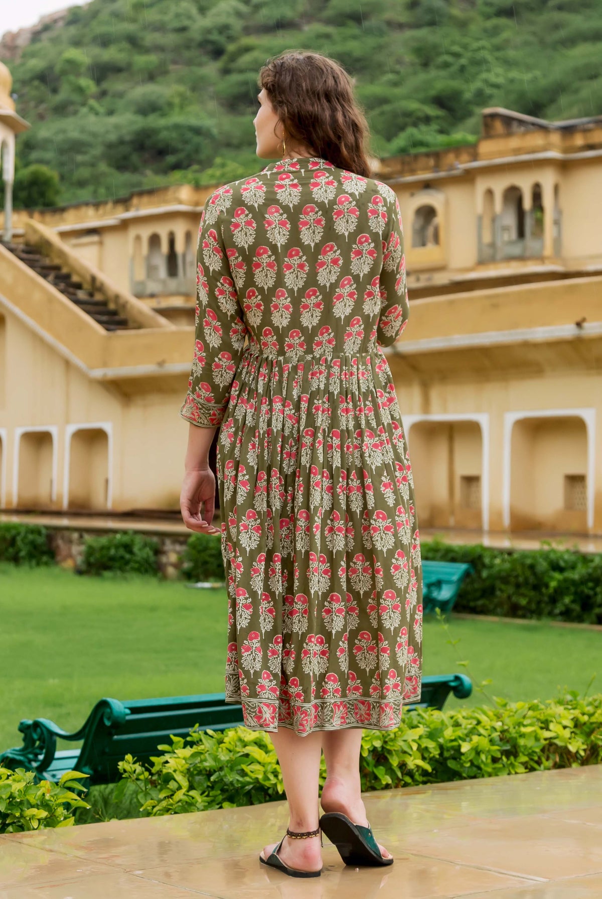 Back view of model in olive green hand block printed dress with red floral patterns.