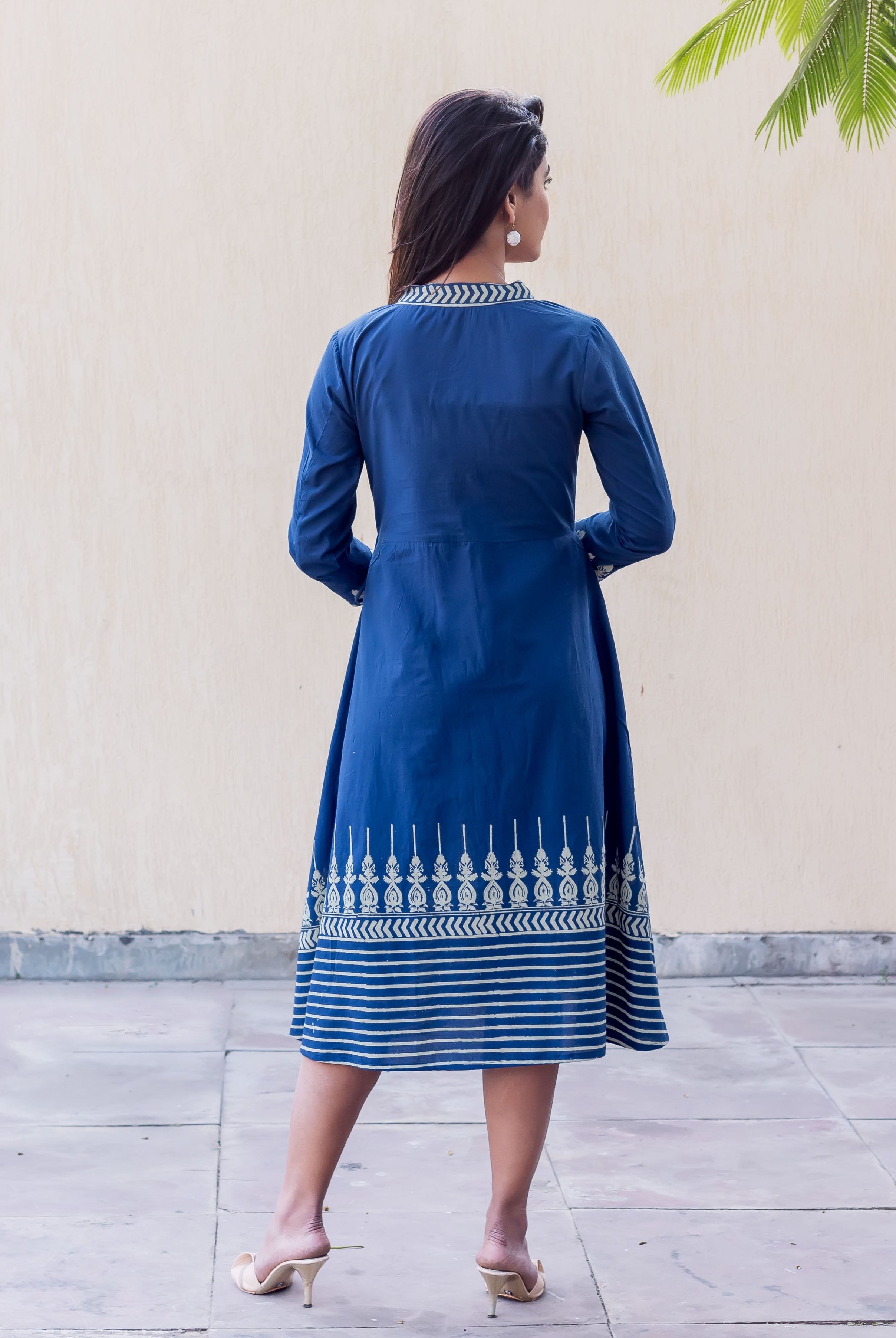 Woman in indigo blue midi dress from back, with white patterned collar and panel print hem.
