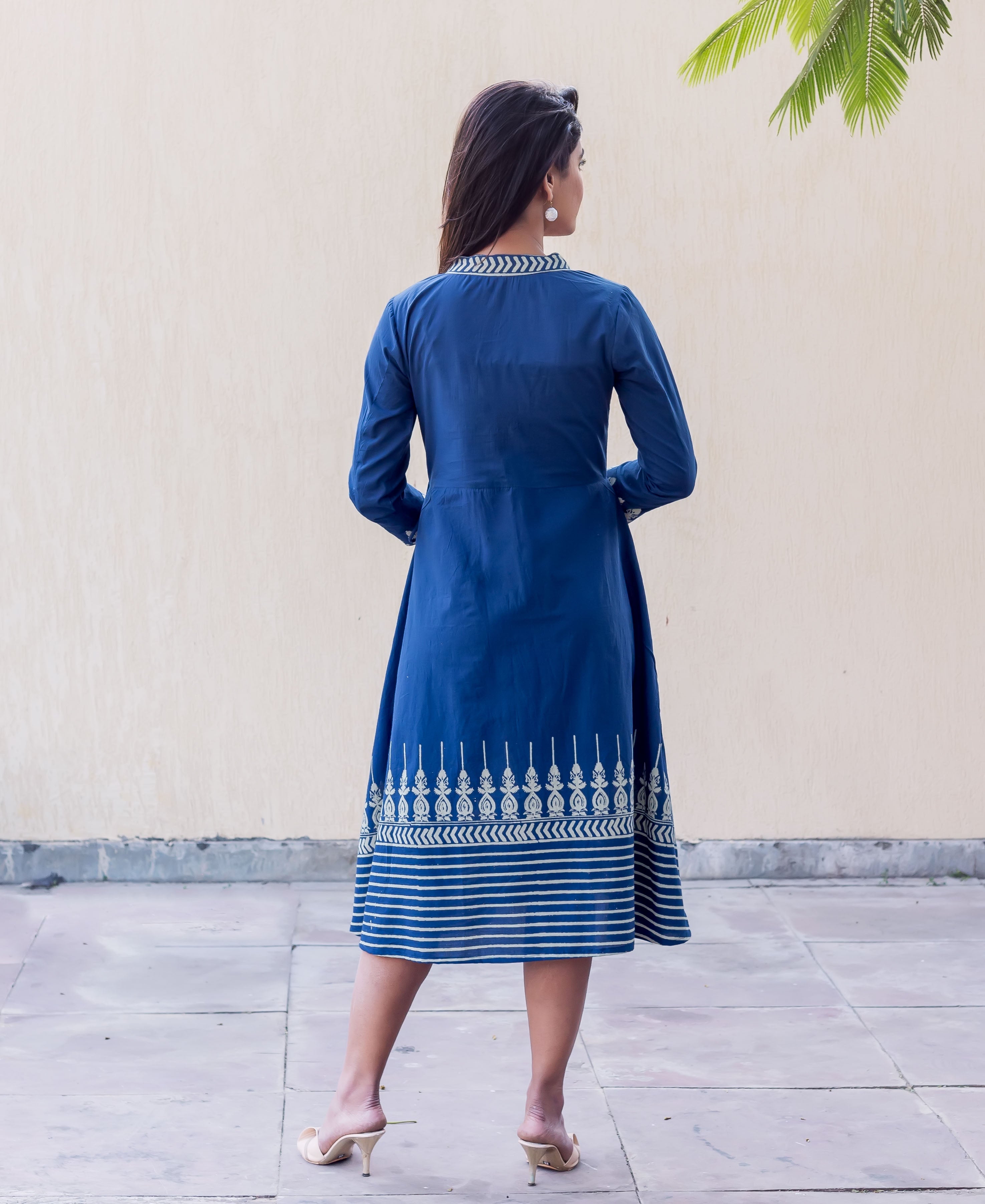 Woman in indigo blue midi dress from back, with white patterned collar and panel print hem.
