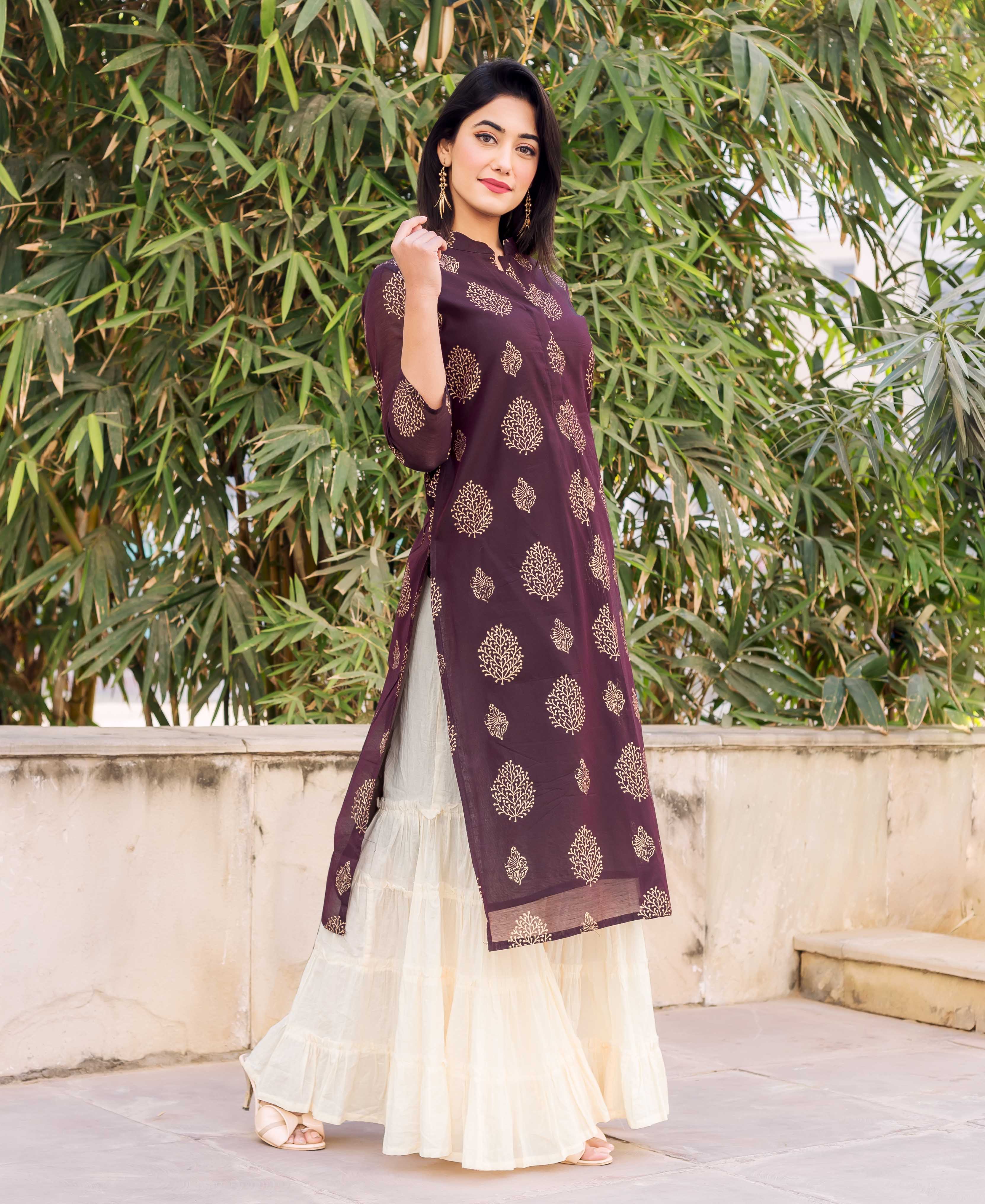 Model wearing a wine kurta with gold leaf print and a creme tiered sharara.