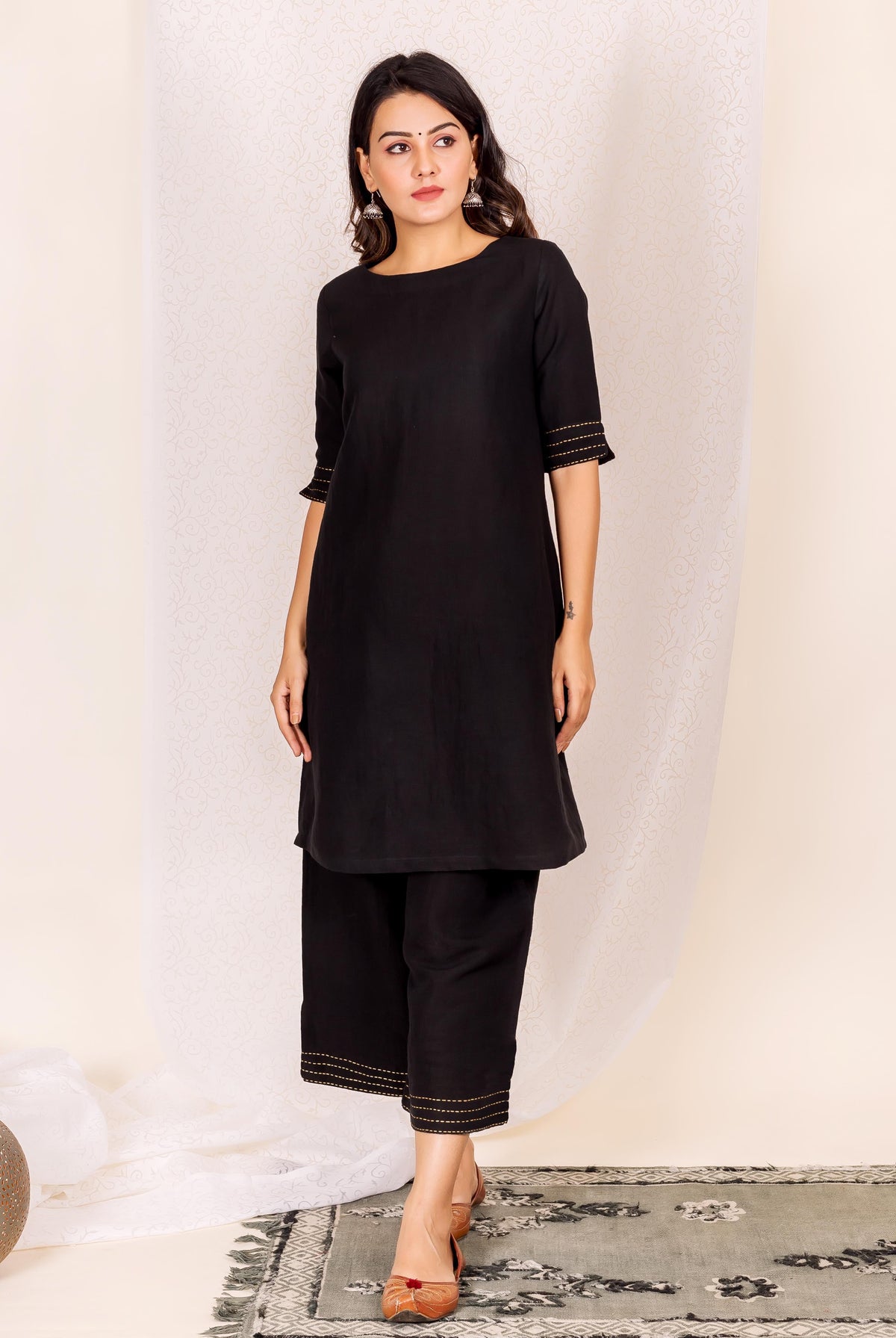 A woman models a black linen kurta with gold accents.