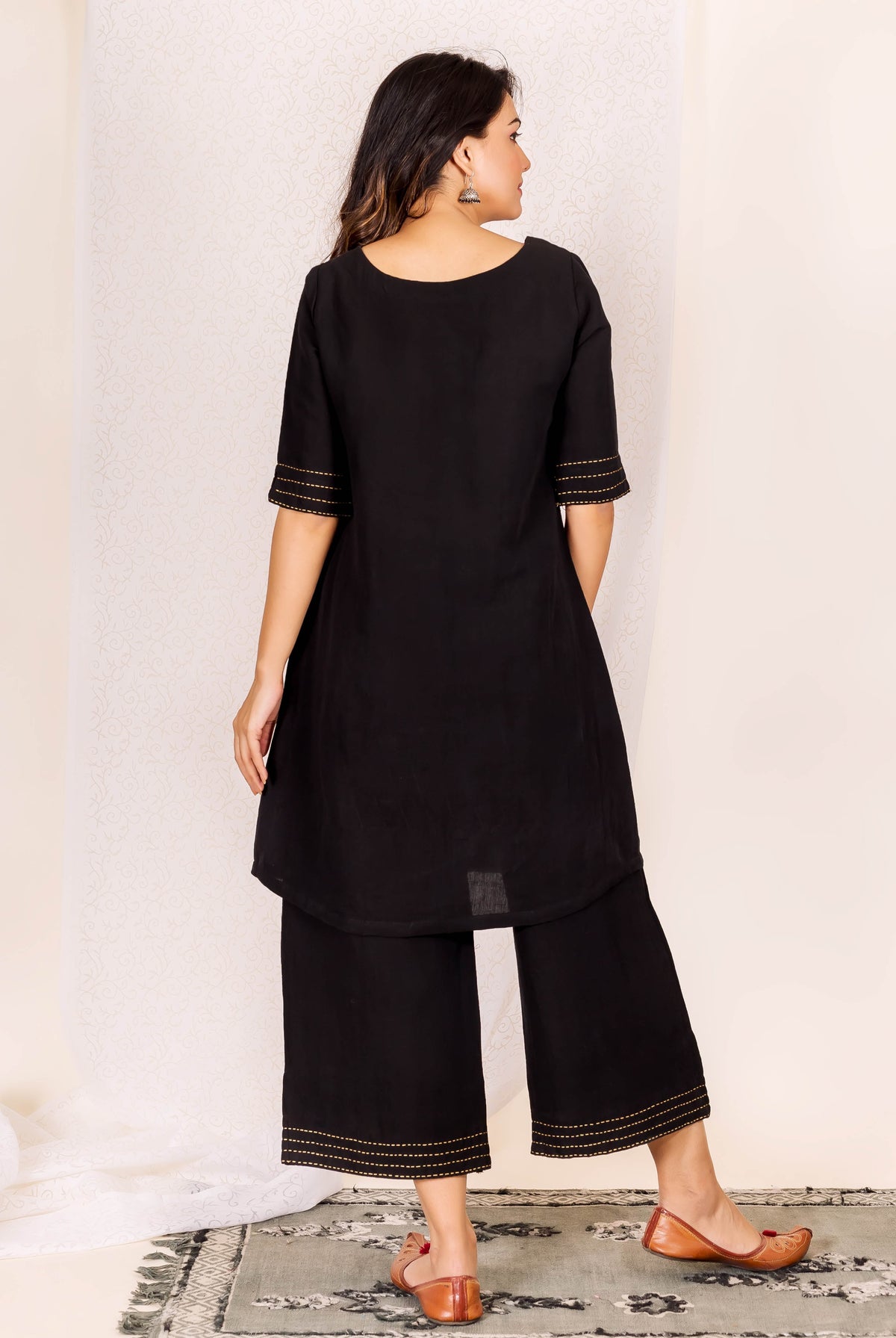 Model's back view wearing black linen kurta set with golden stitch details on sleeves and hems.