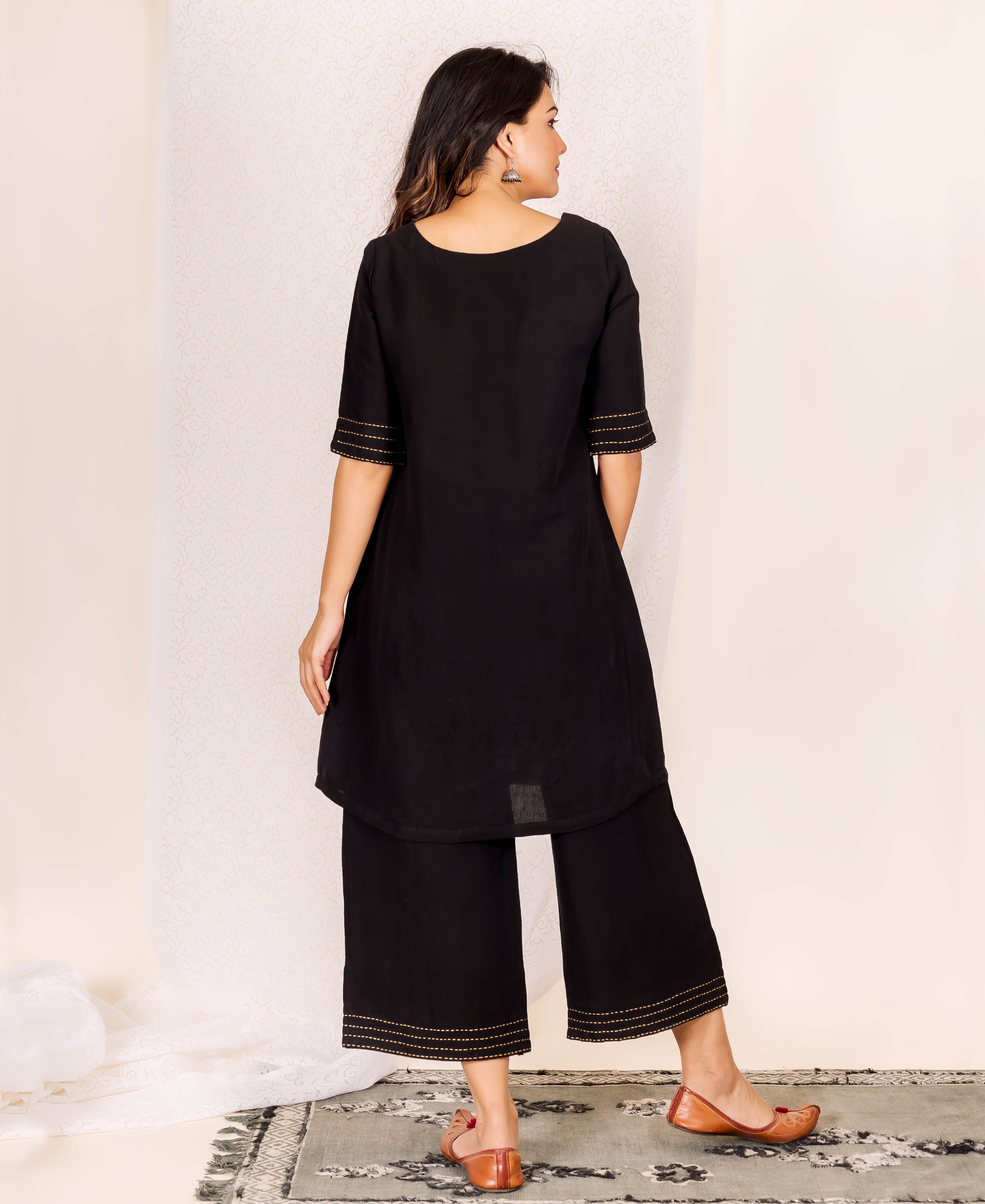 Model's back view wearing black linen kurta set with golden stitch details on sleeves and hems.