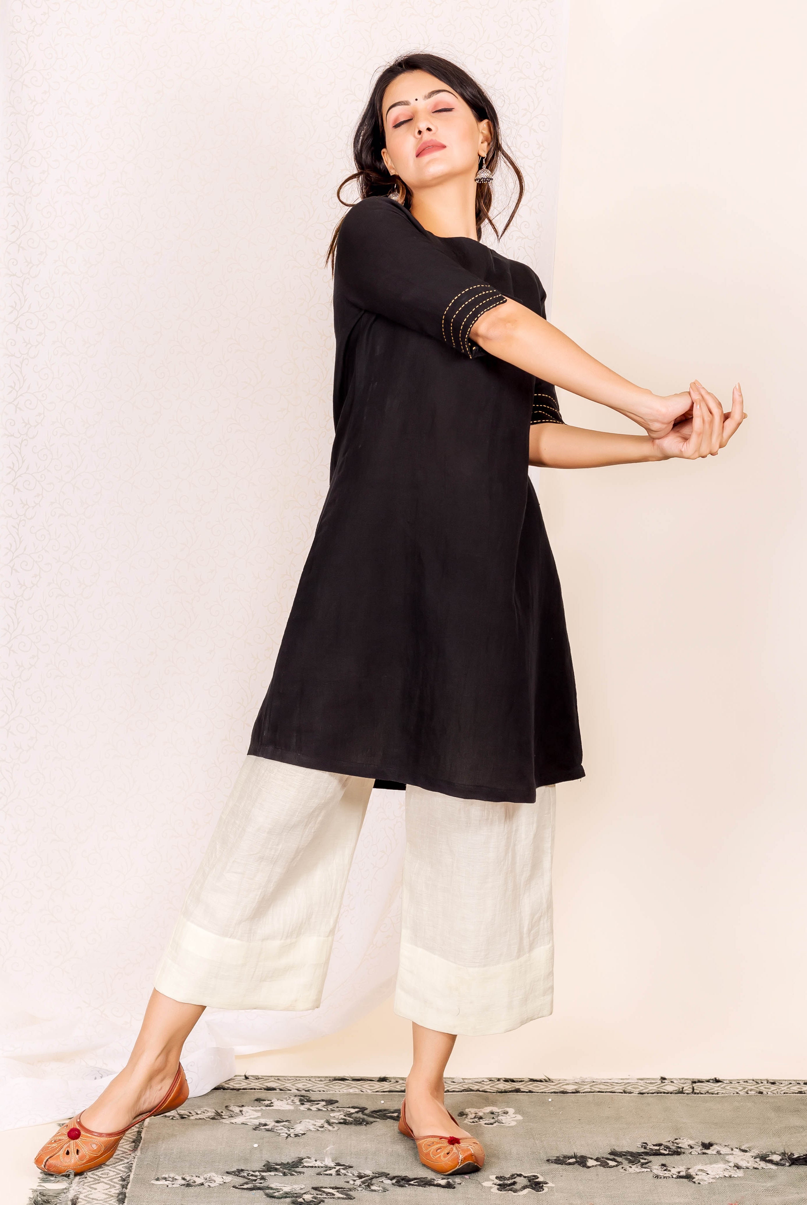 Model in black linen kurta with gold embroidered sleeves and off-white wide-leg pants.
