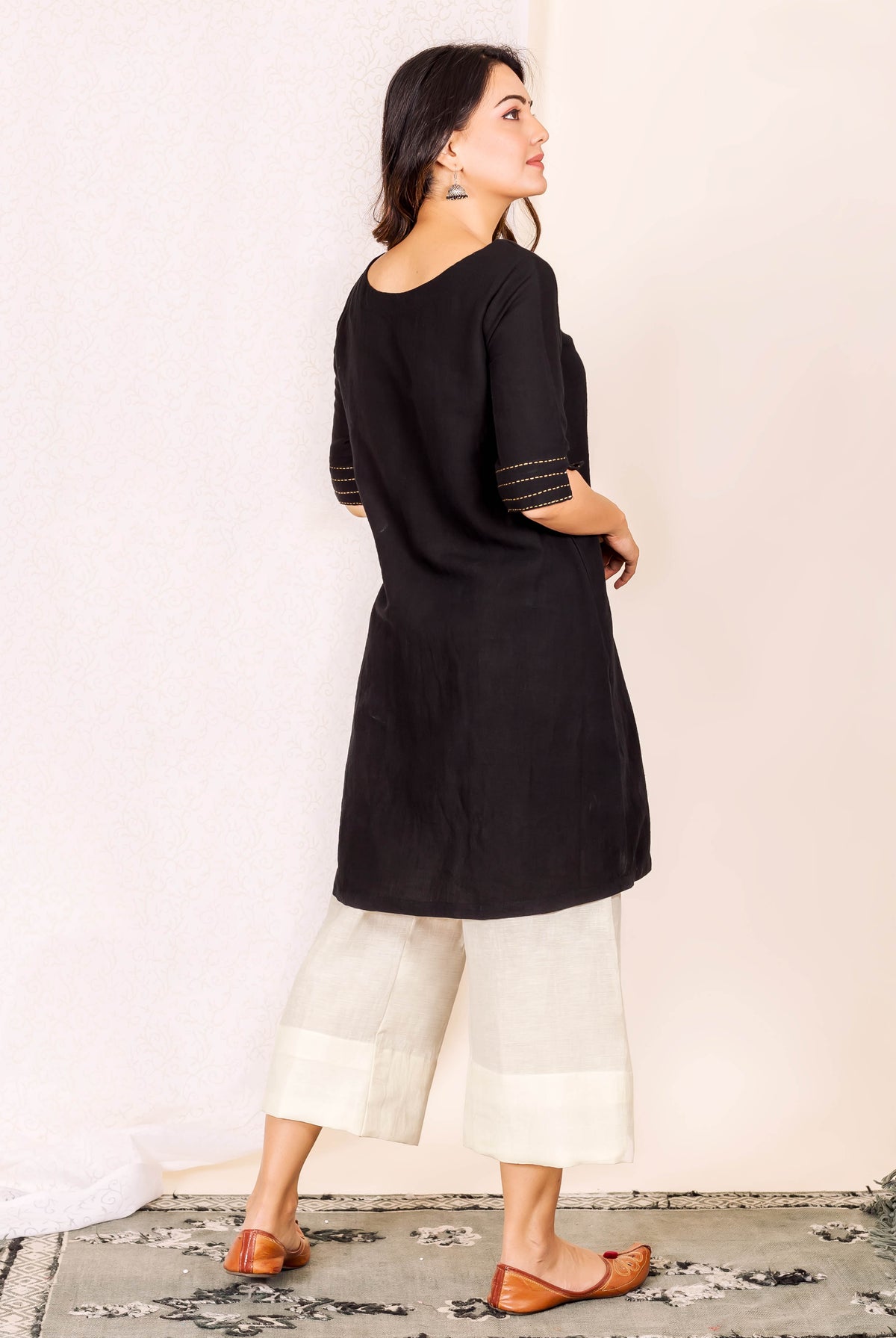 Black kurta with golden stitching on sleeves and off-white pants, worn by model looking right.