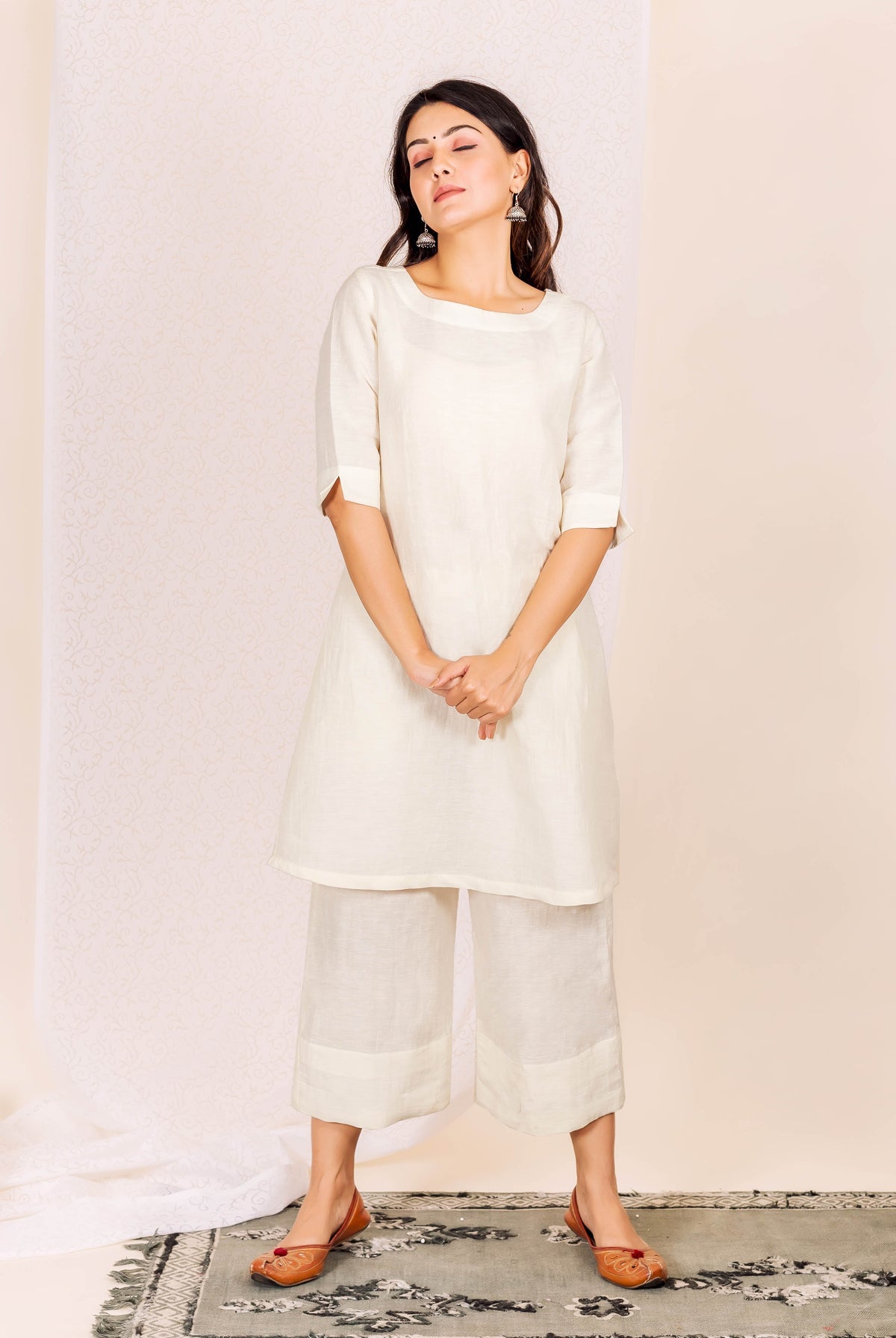 Full shot of a woman modeling a plain off-white linen boat-neck ethnic kurta set.