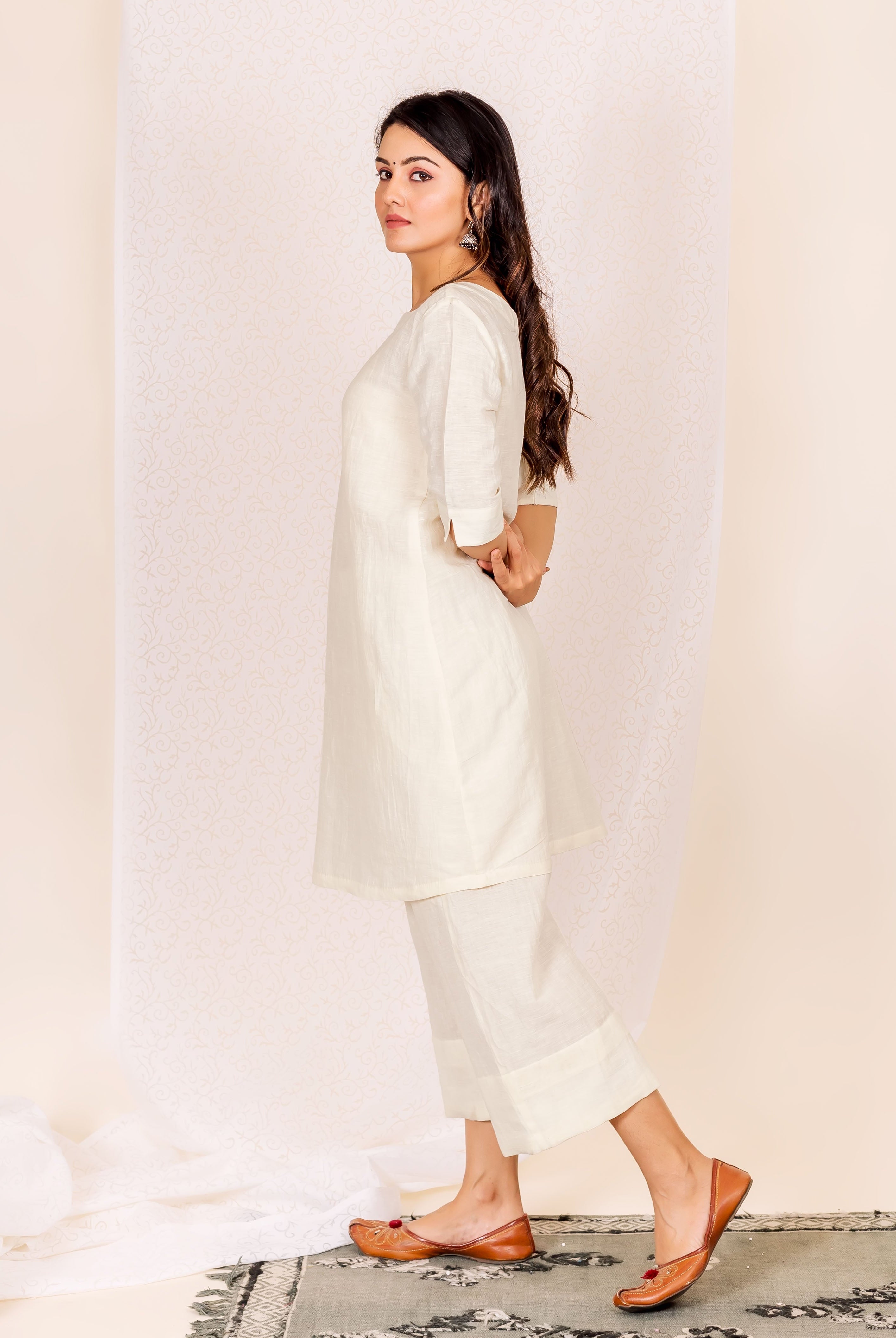 Model wearing an off-white linen ethnic kurta set, looking back at camera.
