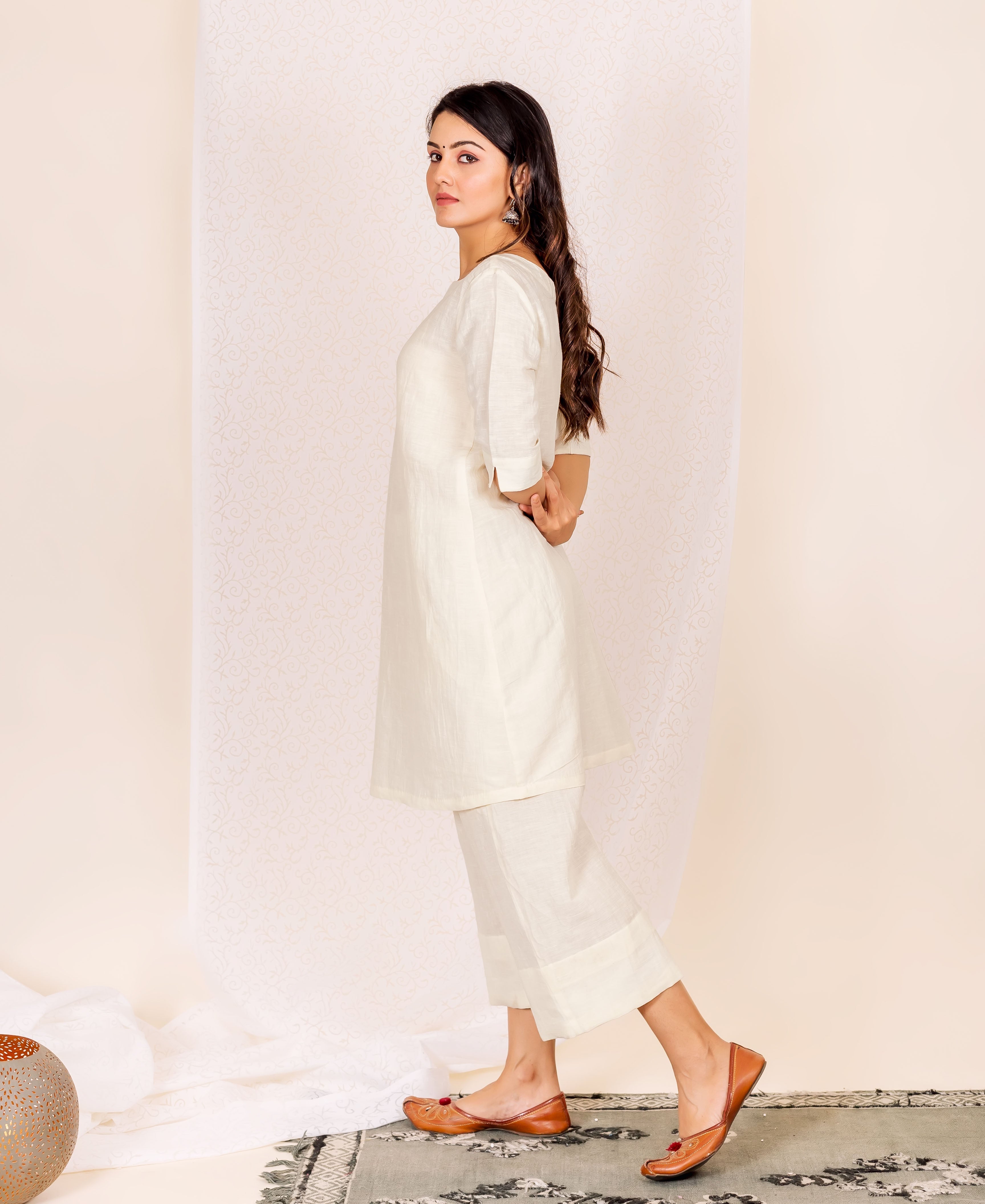 Model wearing an off-white linen ethnic kurta set, looking back at camera.