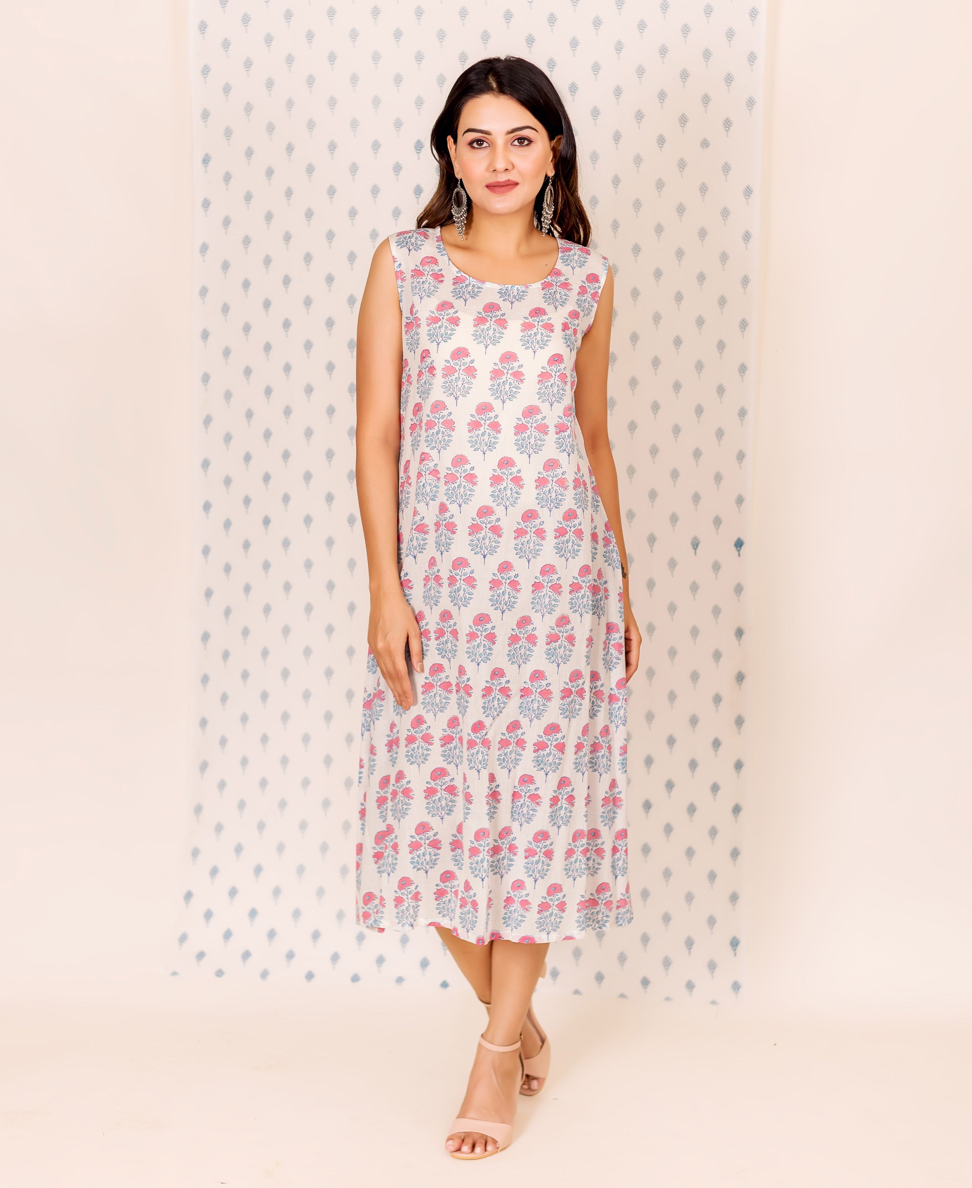 Front view of model wearing a sleeveless cream dress with pink and bluish-grey floral block print.
