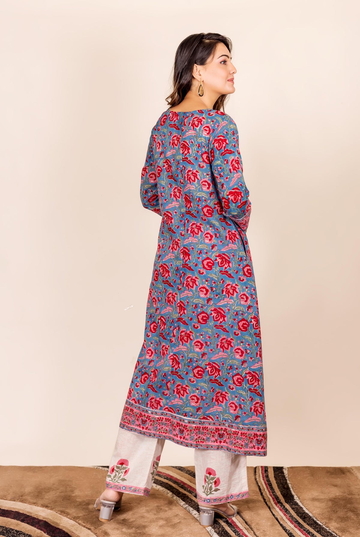 Woman models long-sleeved blue hand block printed kurta with red floral motif and cream pants.