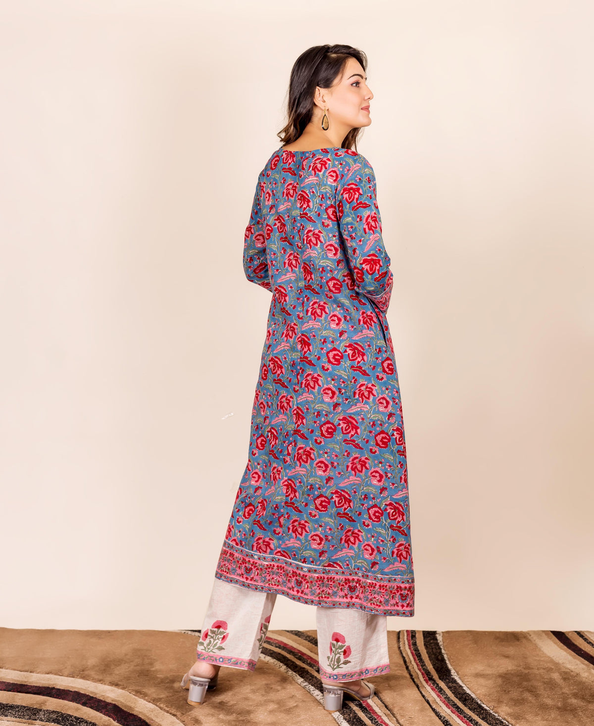Woman models long-sleeved blue hand block printed kurta with red floral motif and cream pants.