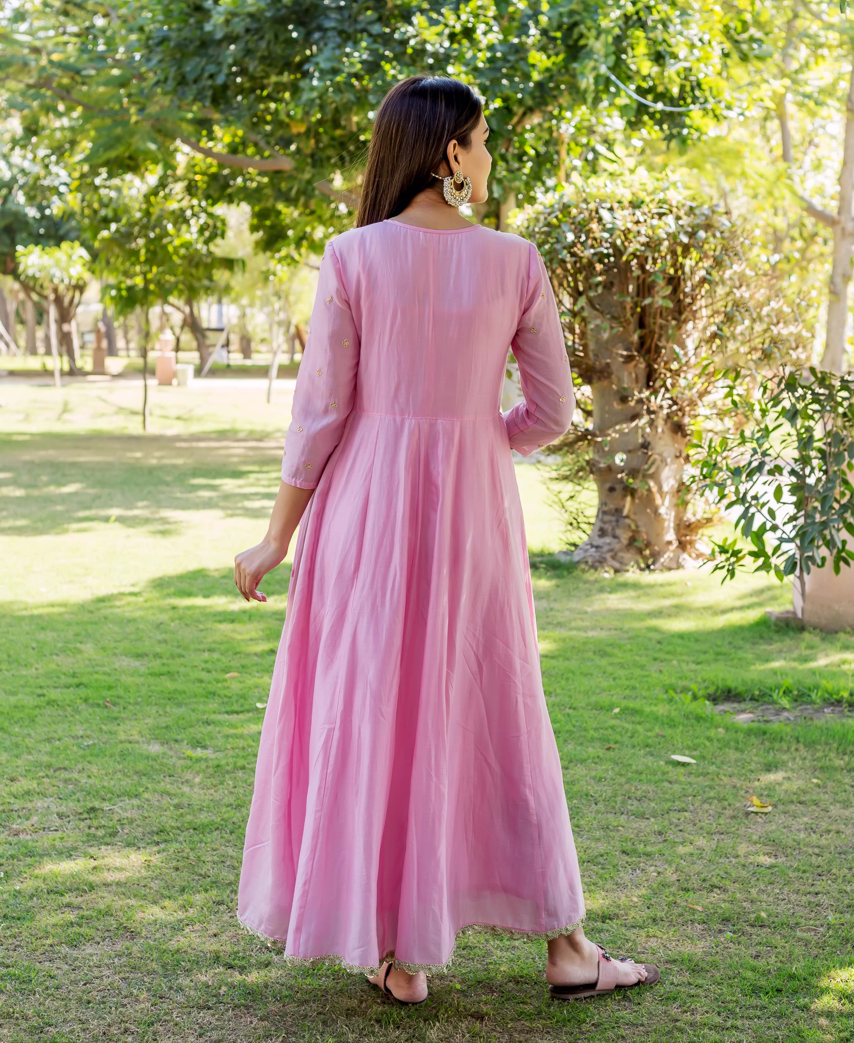 Back view of model in a long blush pink embroidered dress with gold details.
