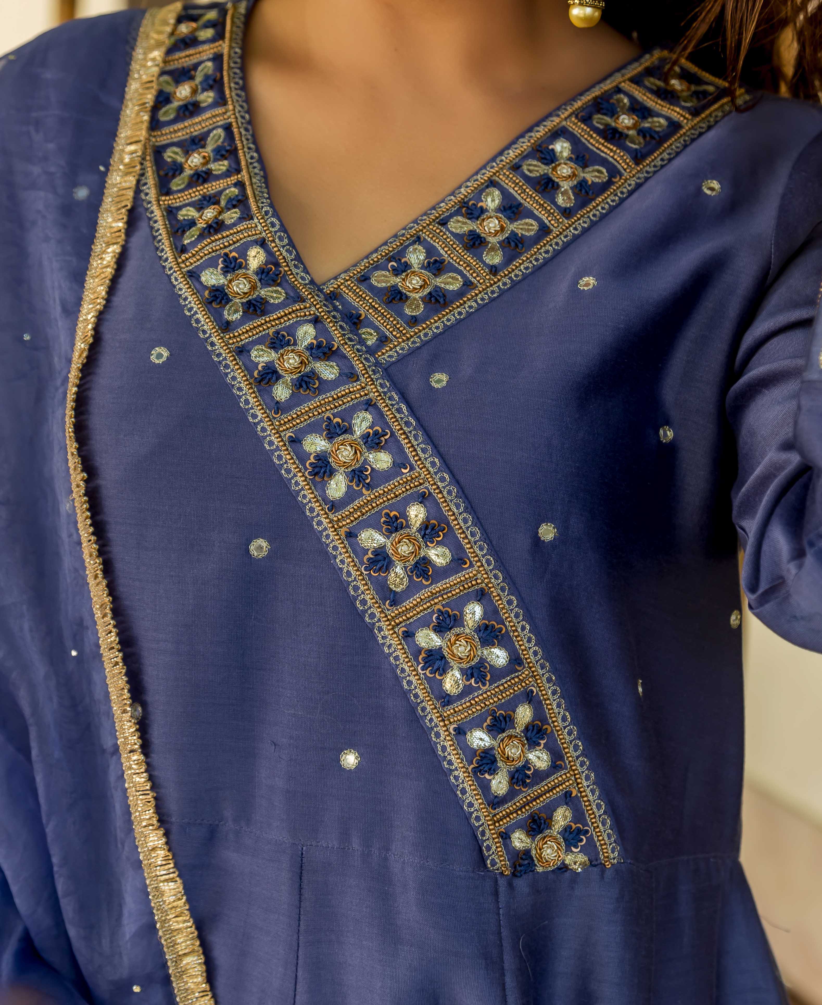 Close-up of model in a steel blue dress with intricate gold and blue embroidered V-neck.