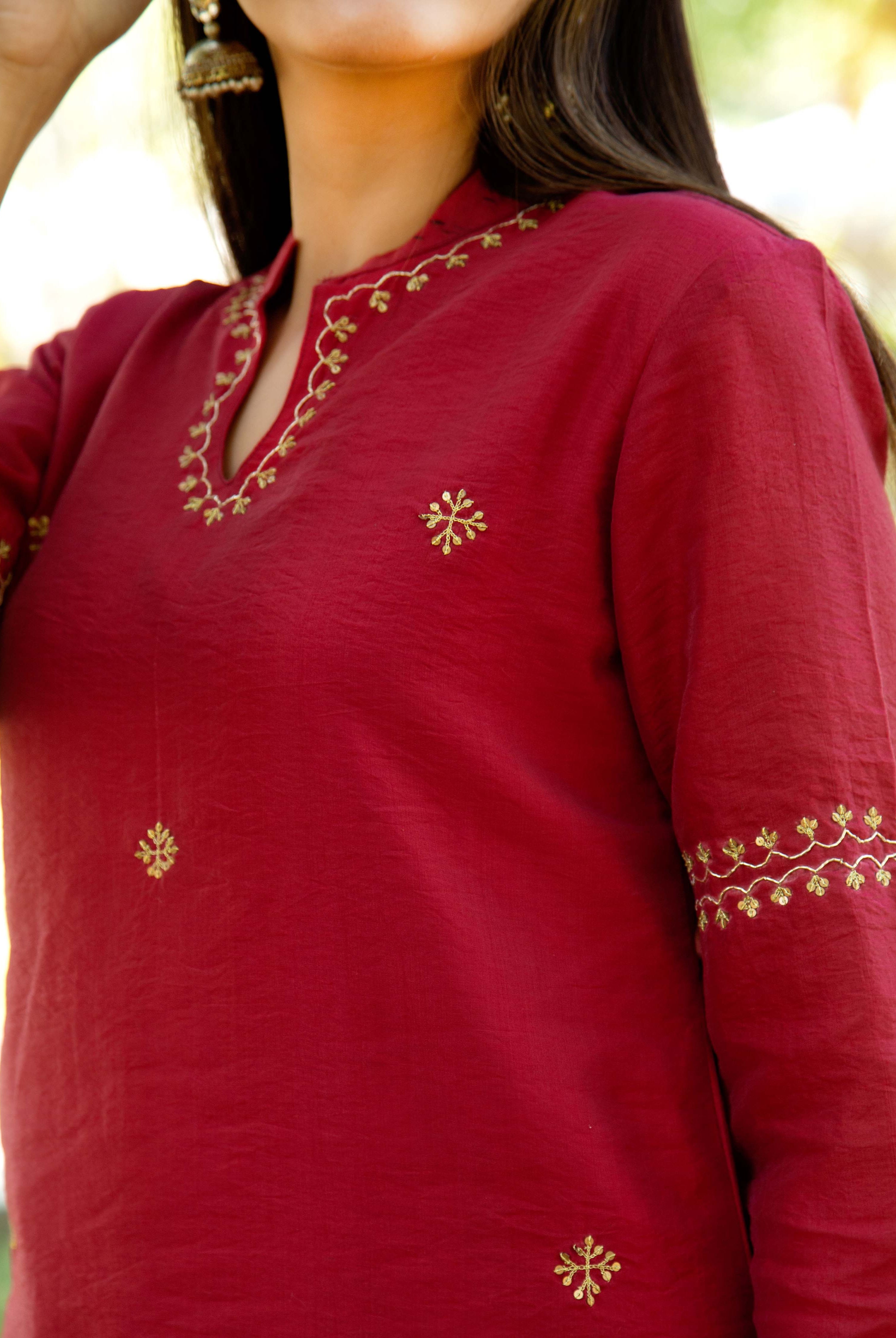 Model wearing a maroon kurta, intricately embroidered with gold patterns on the neckline and sleeves.