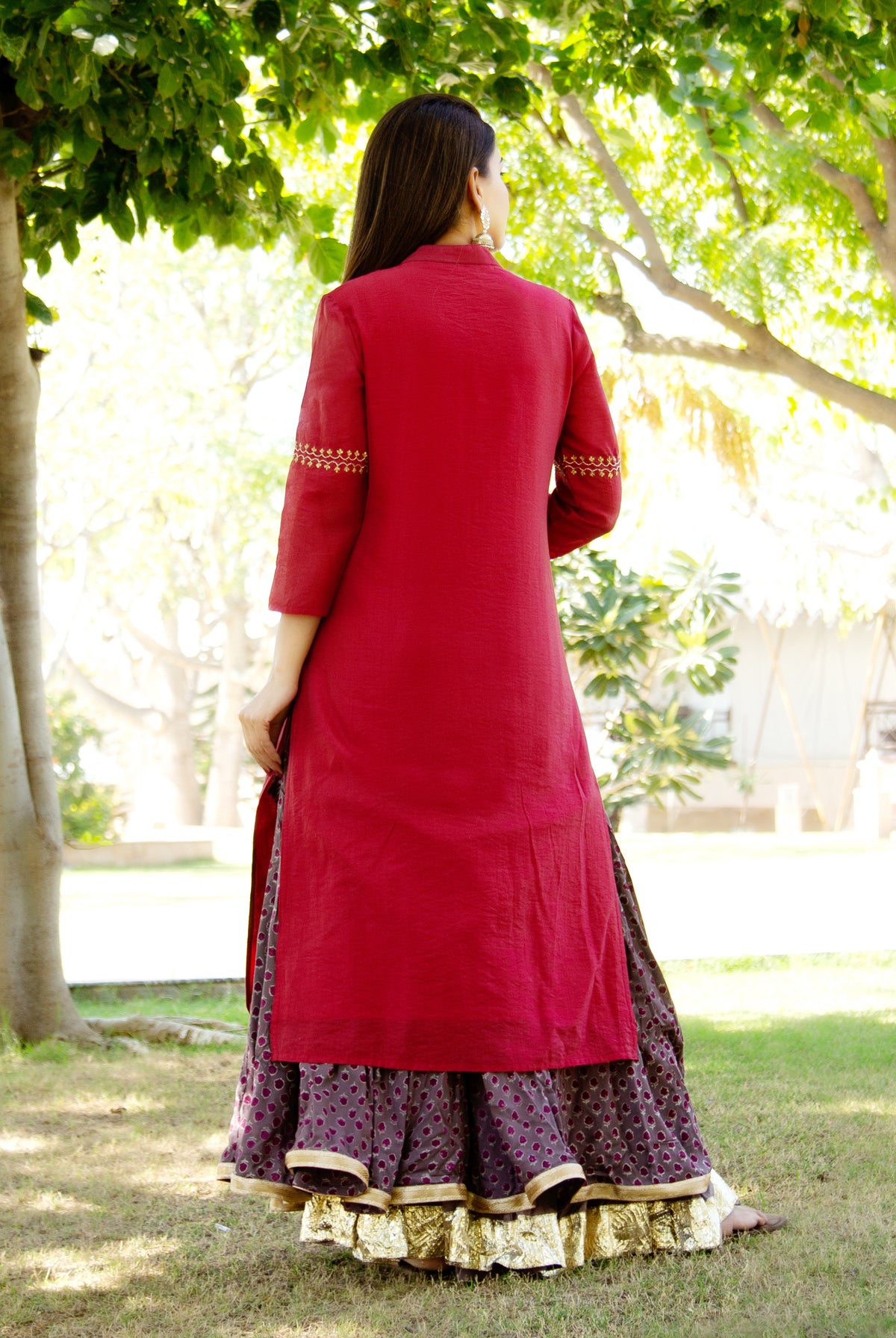 Model from back in maroon embroidered kurta over dark patterned skirt with gold border.
