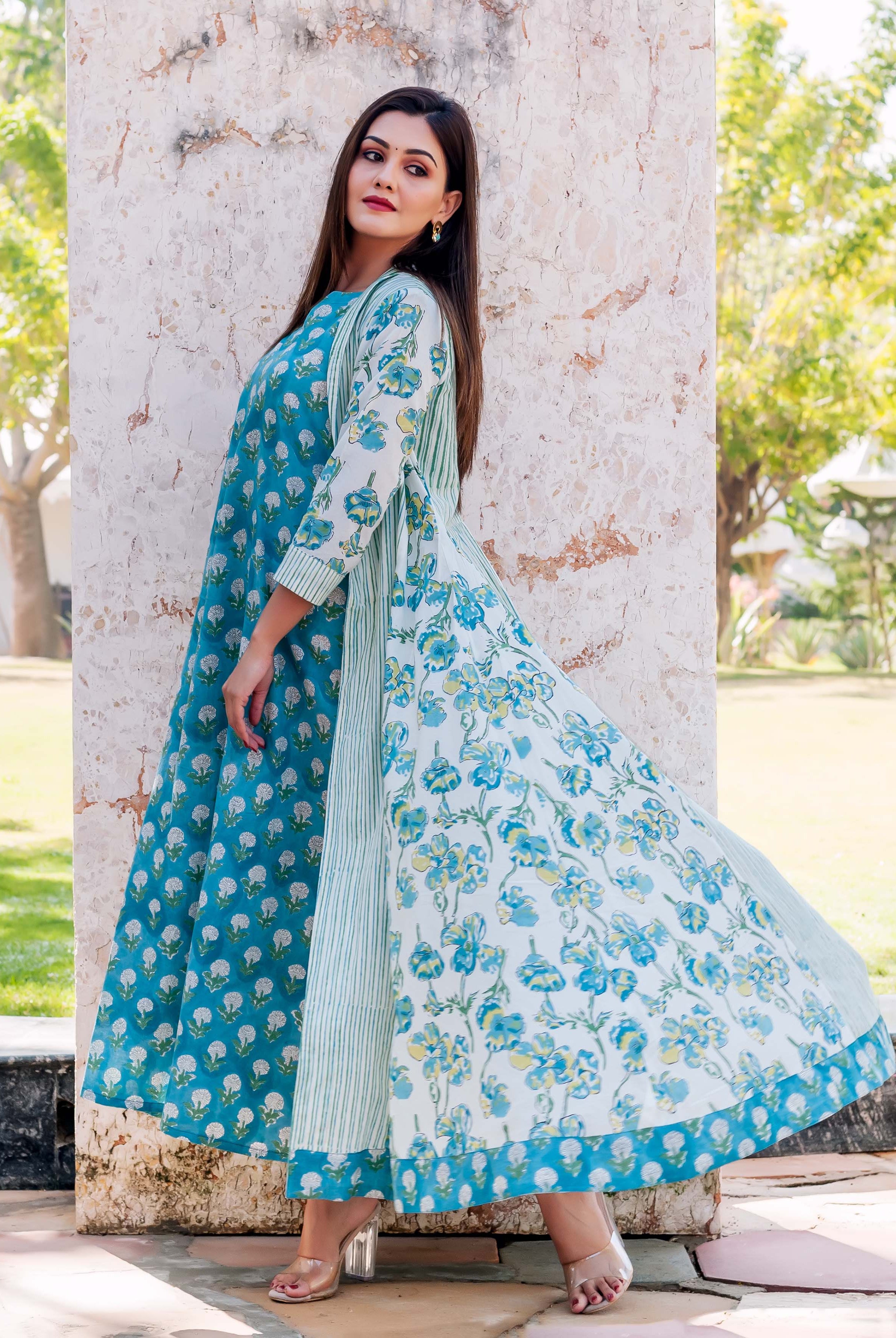 Model in side profile wearing a full blue block print dress and white floral striped jacket.