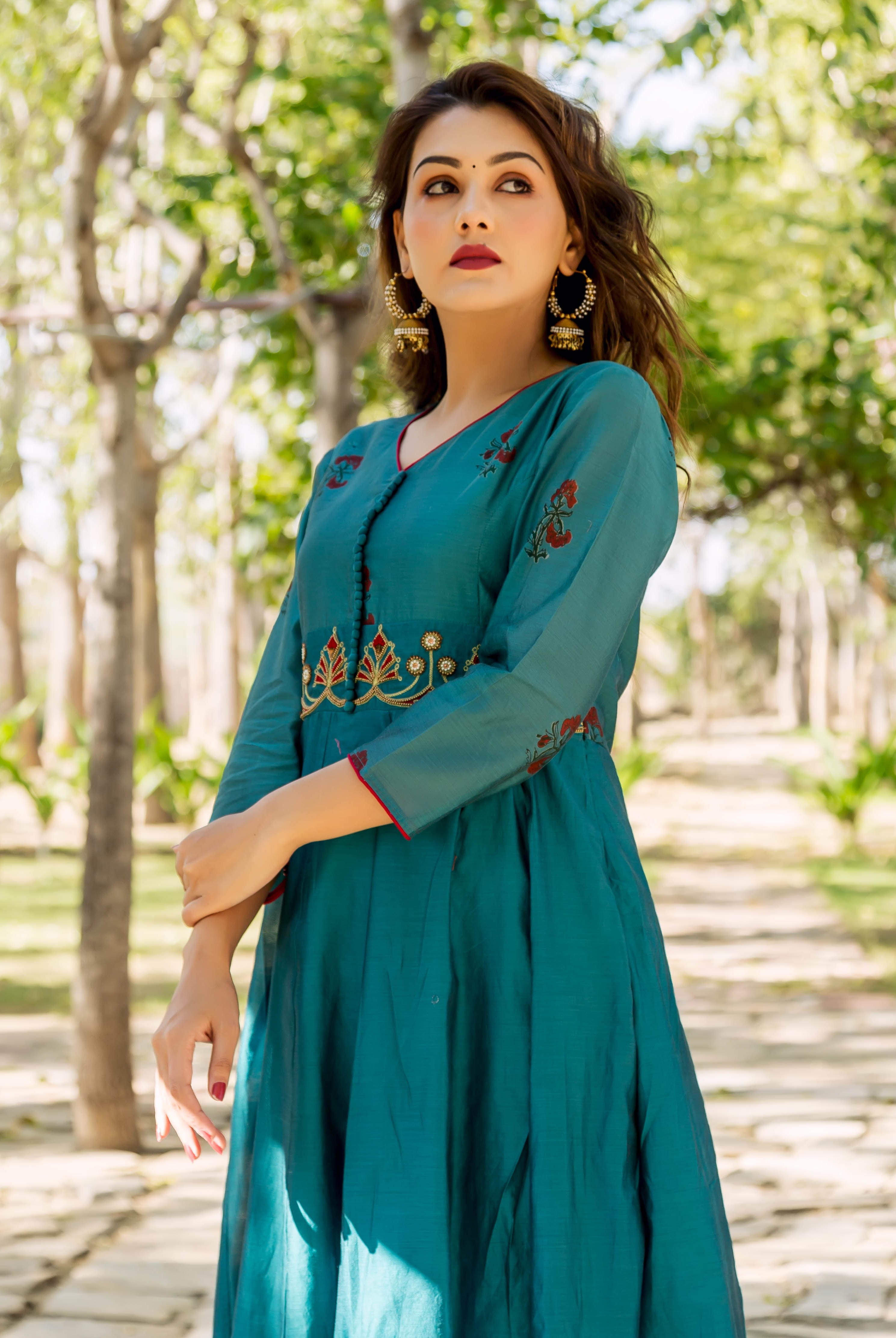 Model poses in a deep teal hand-embroidered kurta, showing intricate yoke and sleeve details.