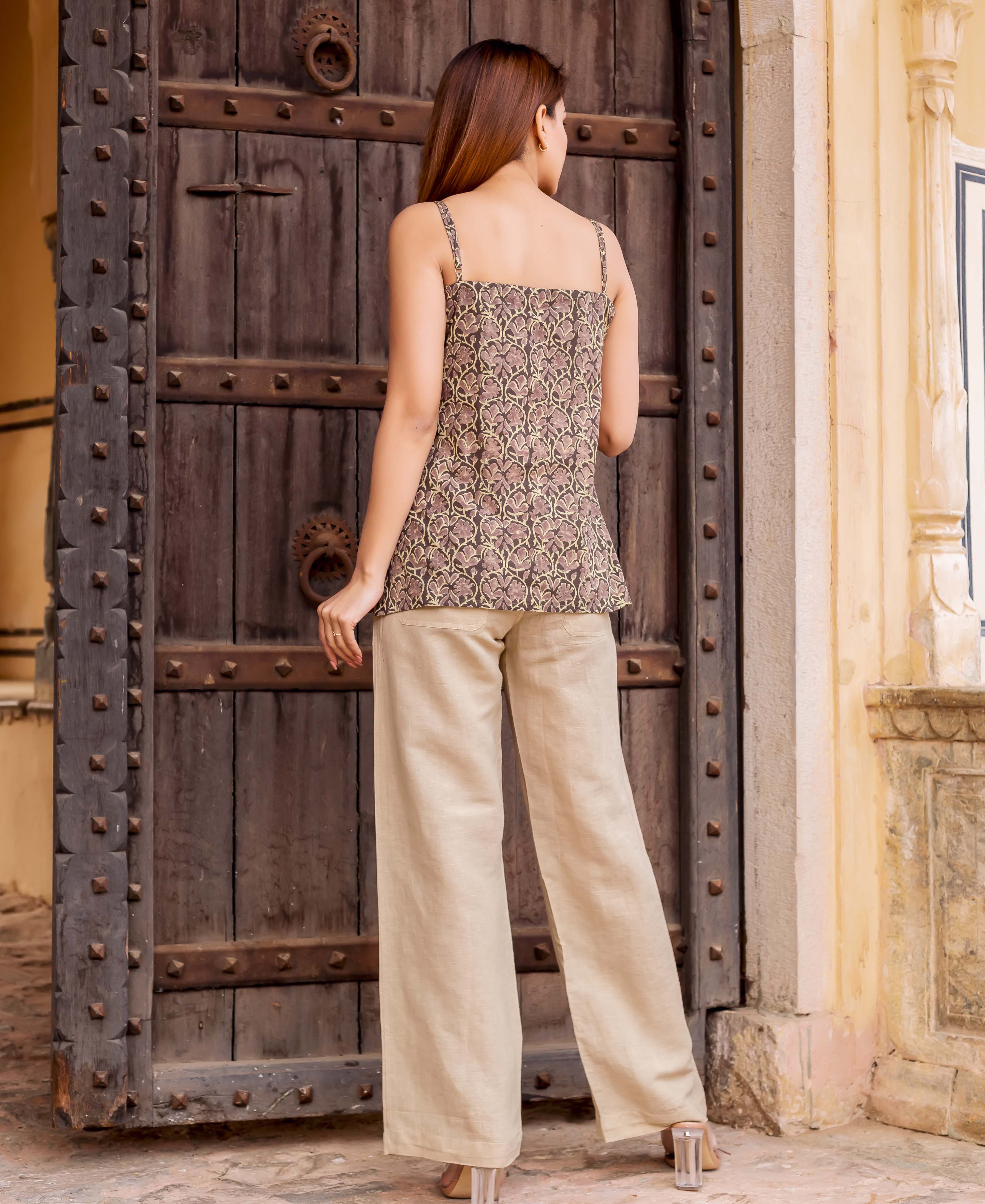 A woman stands in front of a wooden door, wearing a beige linen coordinated set with a floral print.