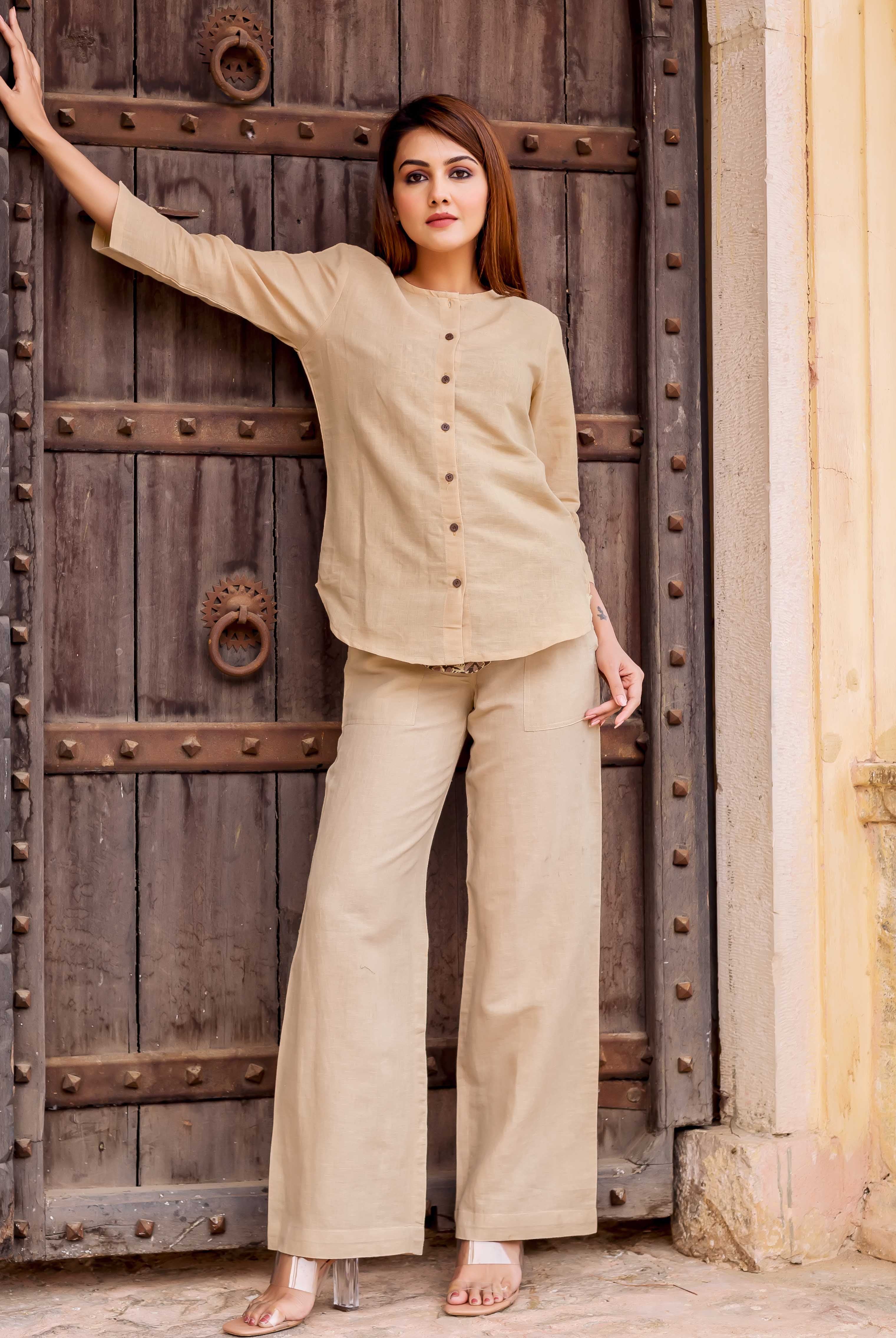A woman in a beige linen coordinated set stands in front of a wooden door.
