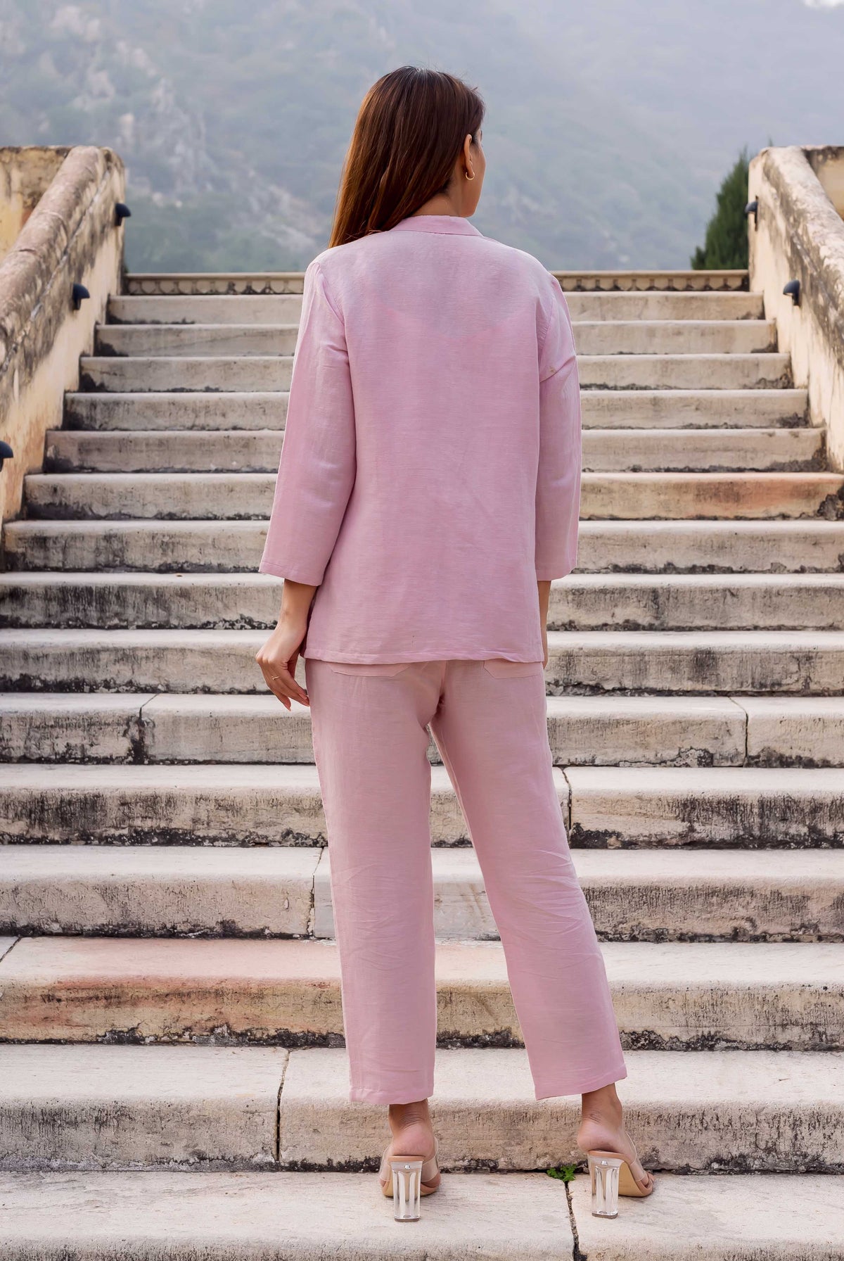 Back view of model in flamingo pink linen coordinated set, standing on stone stairs.