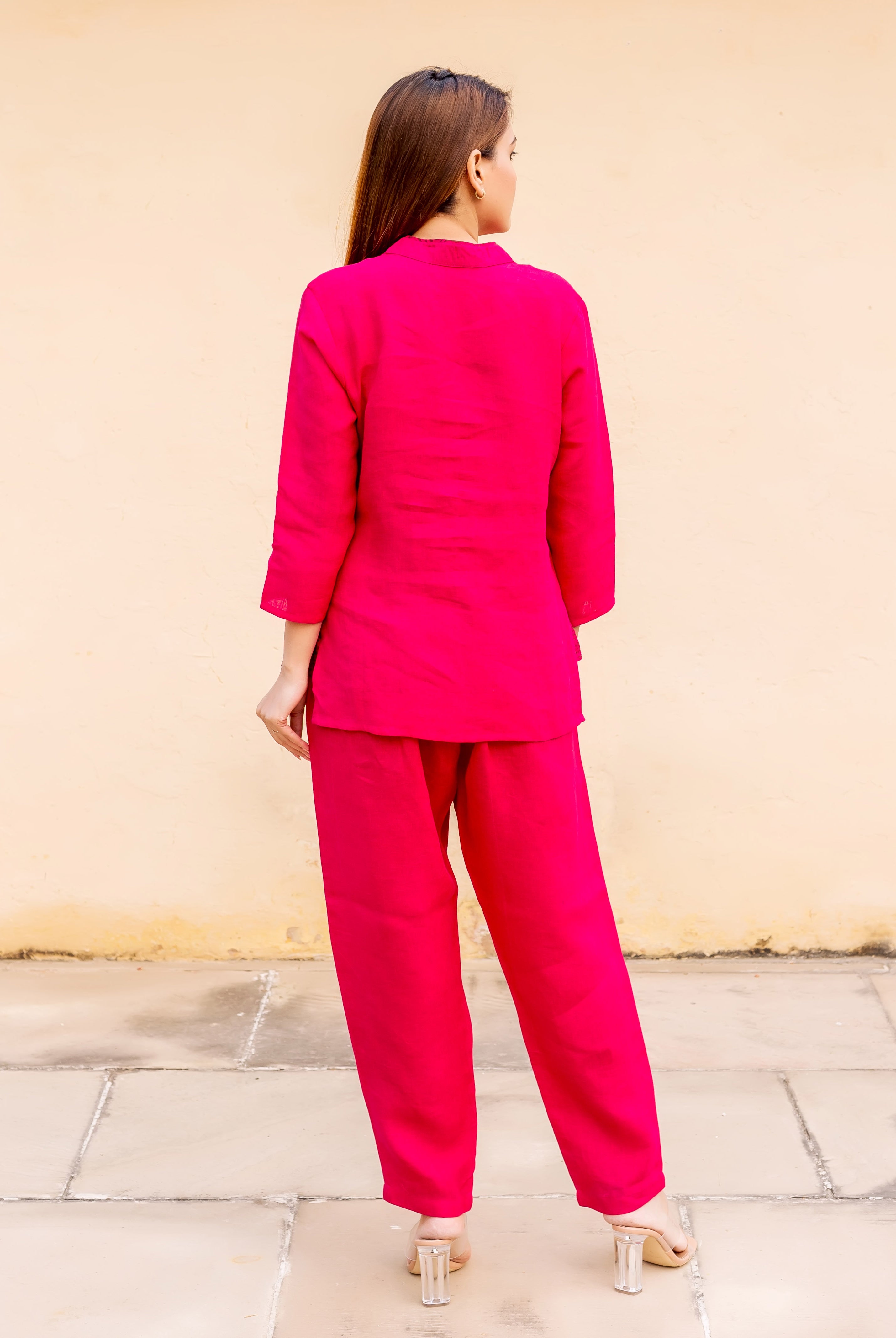 Model from behind in a ruby pink linen power suit, looking over right shoulder.