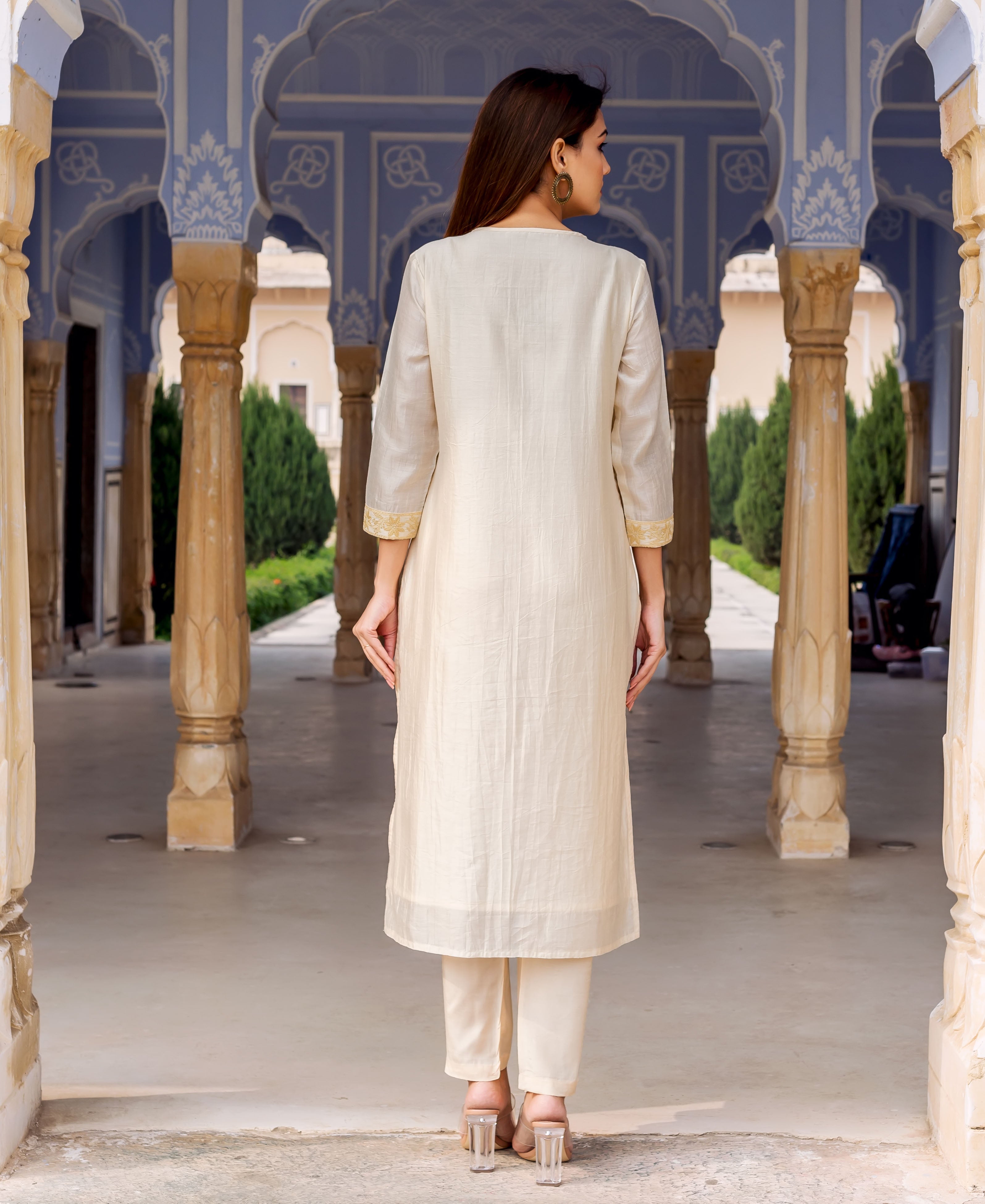 Model from behind in a cream straight kurta and pants featuring subtle golden embroidery.