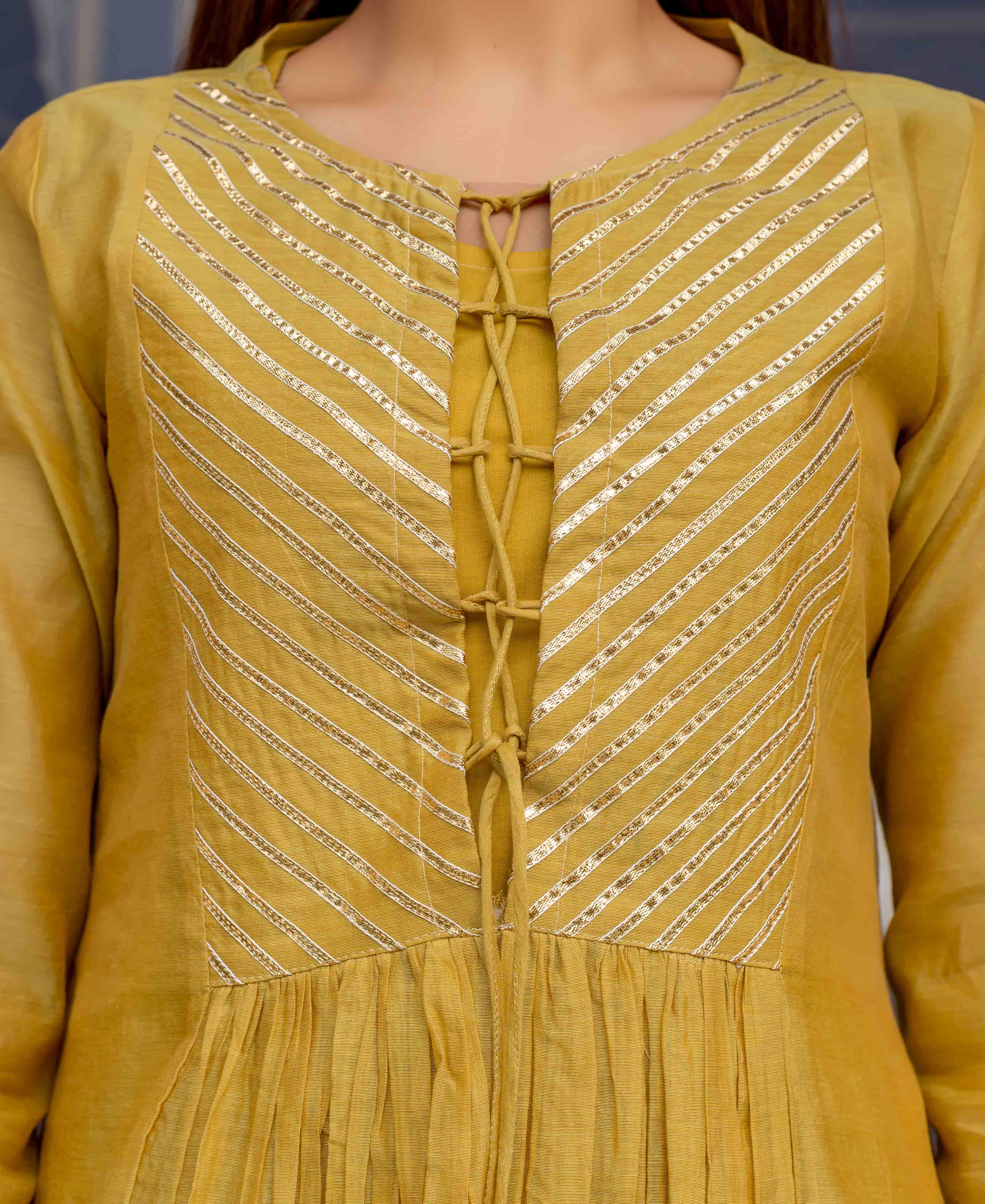 Model wearing honey yellow kurta with diagonal gold gota work and decorative front lacing.