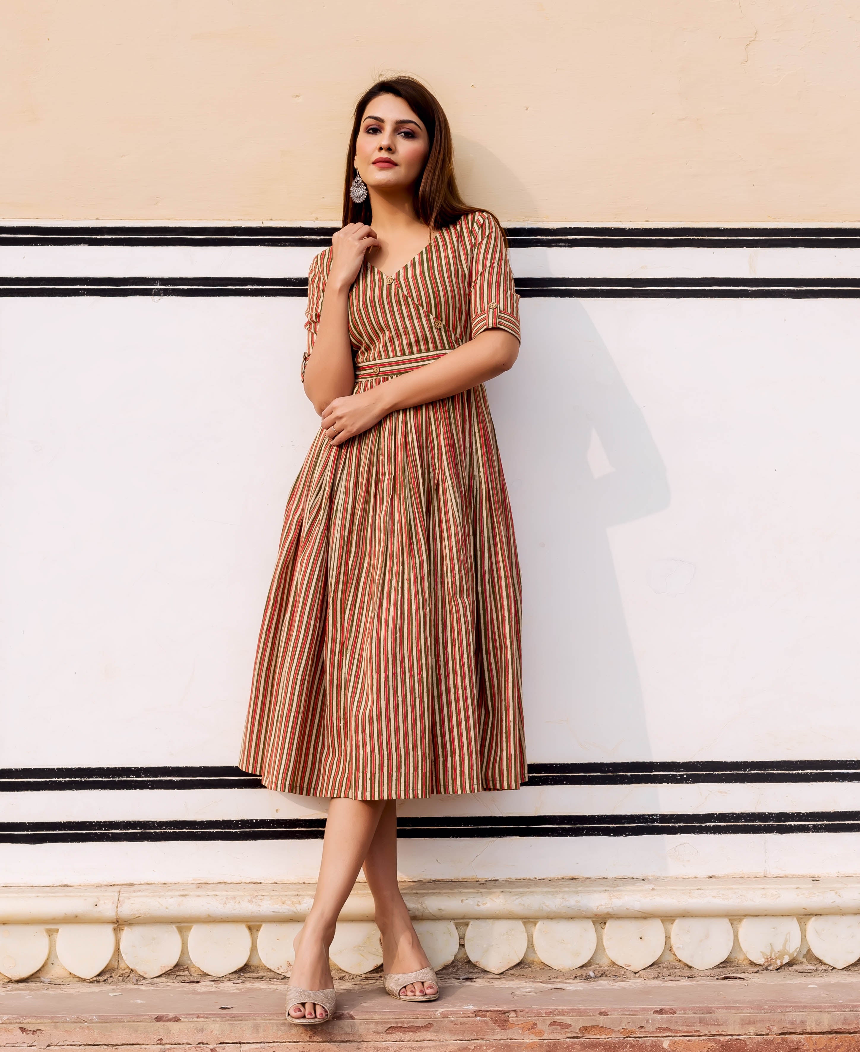 Woman wears an olive and red striped hand block printed sundress standing against a wall.