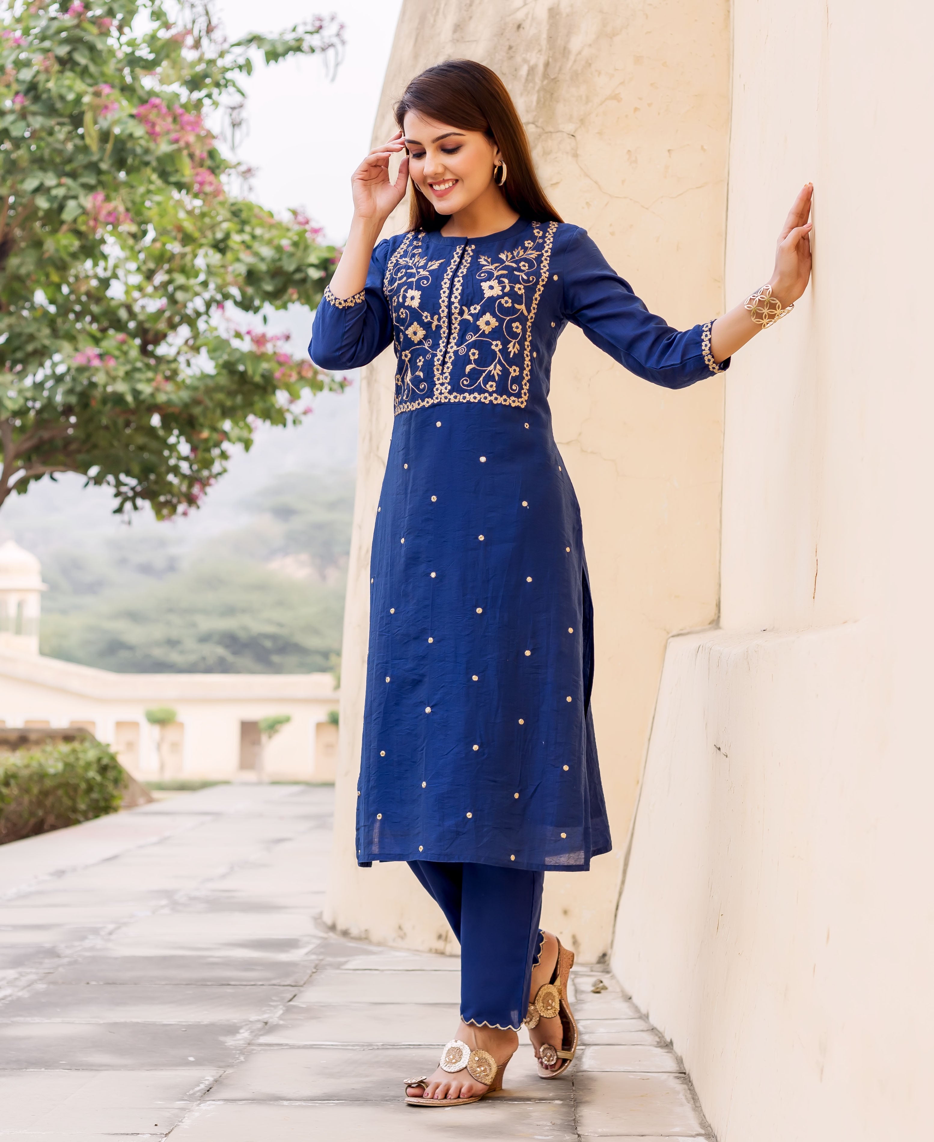 Woman modeling a midnight blue hand-embroidered kurta set with gold floral design and small dots.