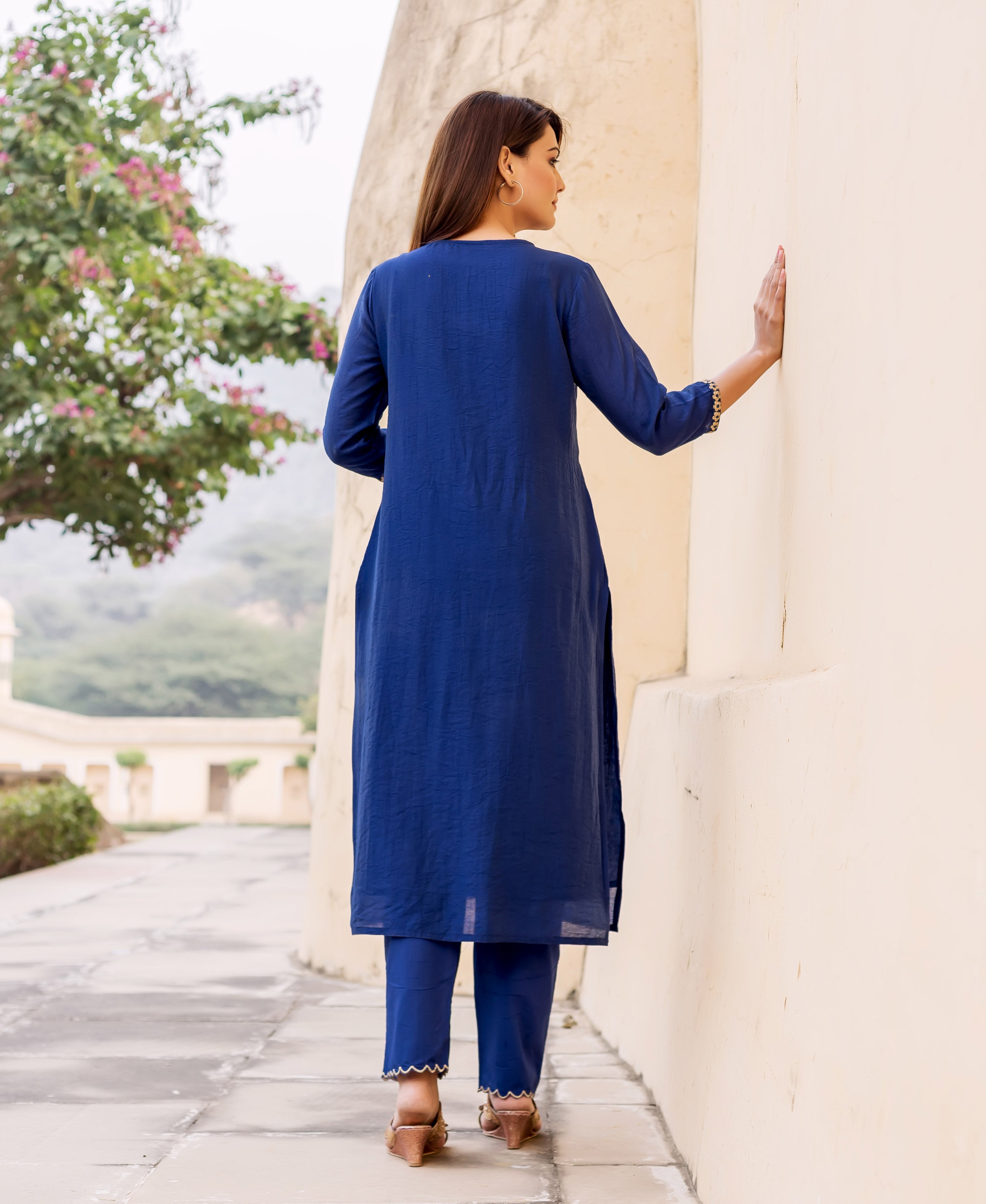 Back view of model in midnight blue hand-embroidered kurta set with golden trim.