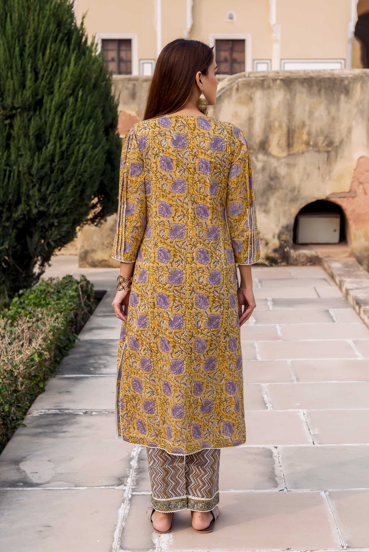 Woman from behind in yellow and purple floral hand block printed kurta with grey chevron pants.